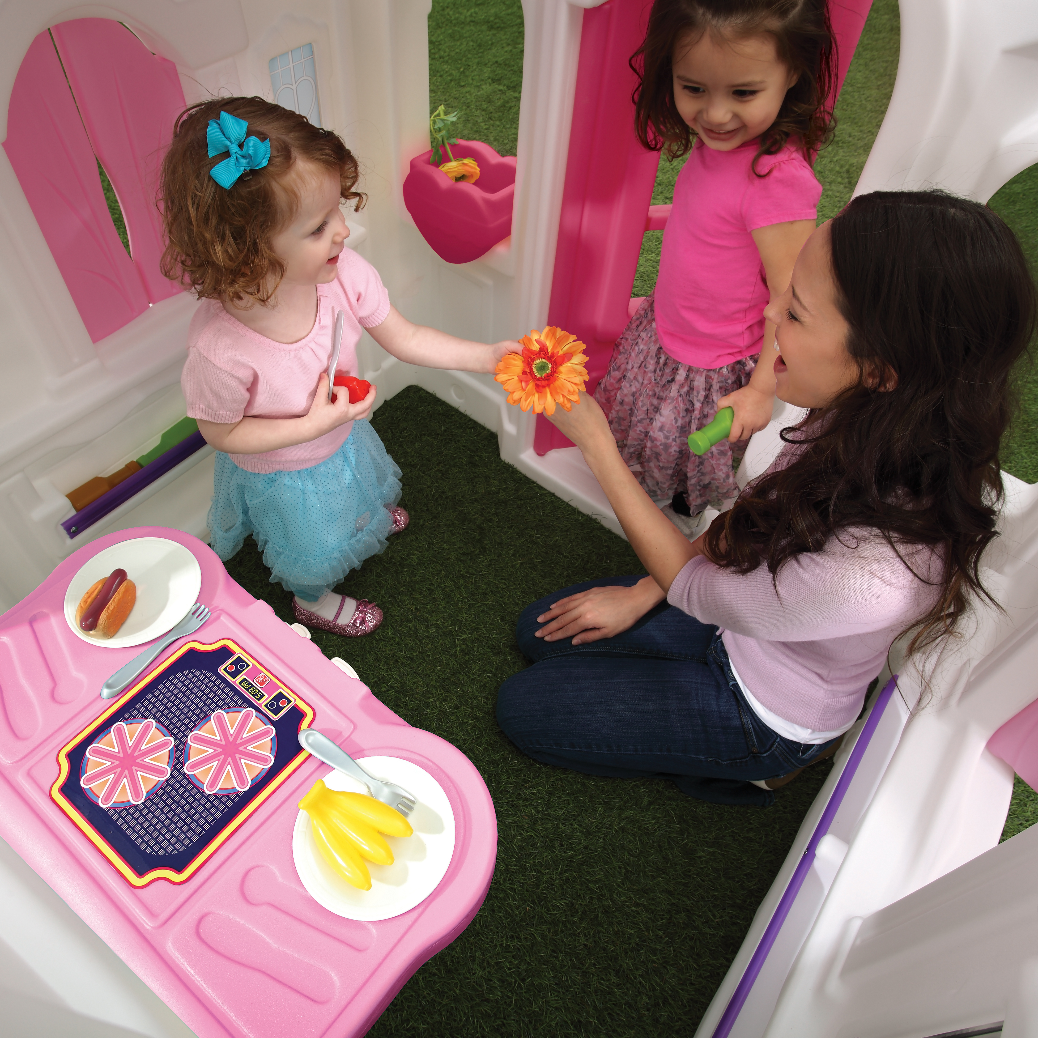 Drei Kinder und ein Erwachsener spielen in einem rosa Spielzeug-Haus.