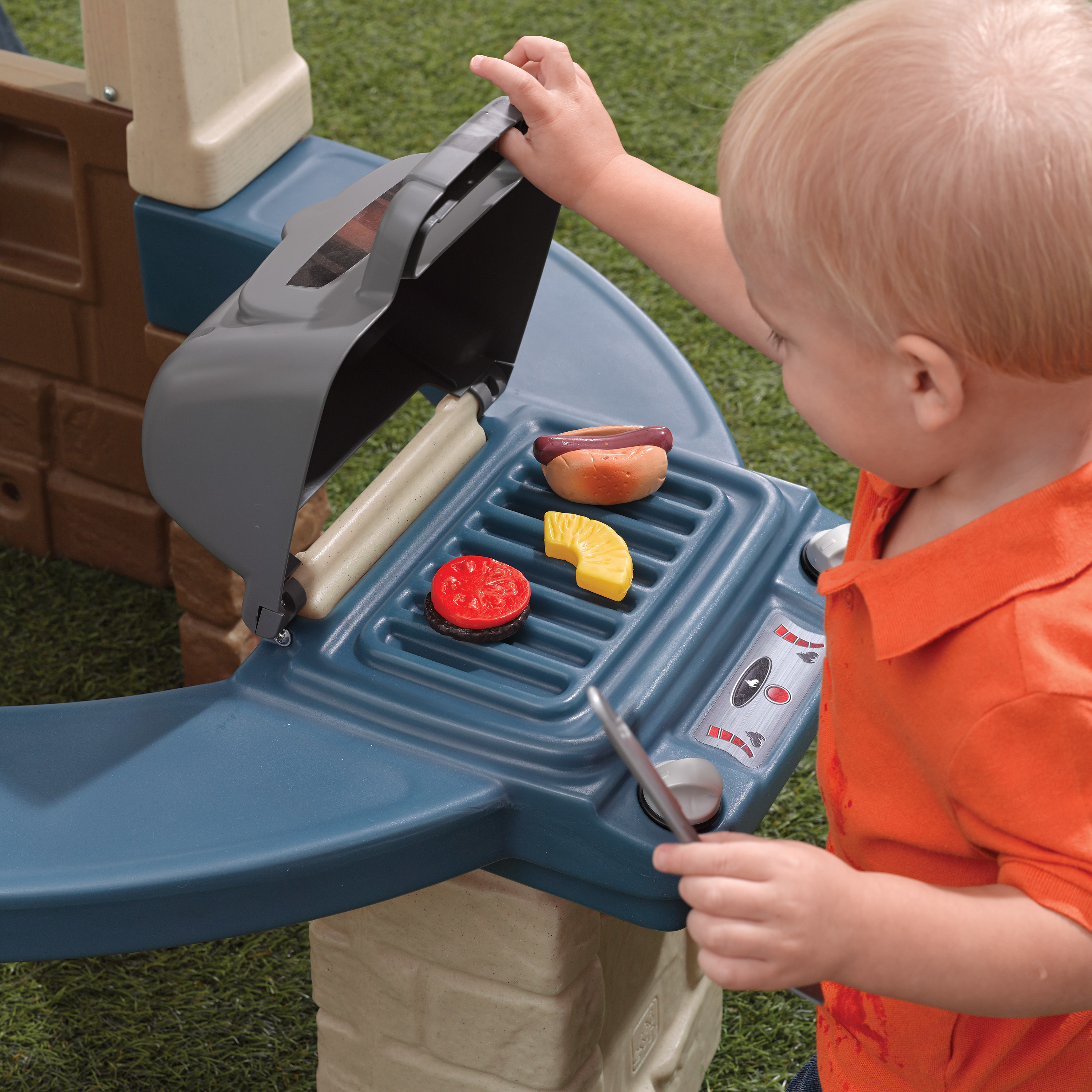 Ein Kind spielt mit einem Spielzeug-Grill. Auf dem Grill befinden sich Spielzeug-Lebensmittel.