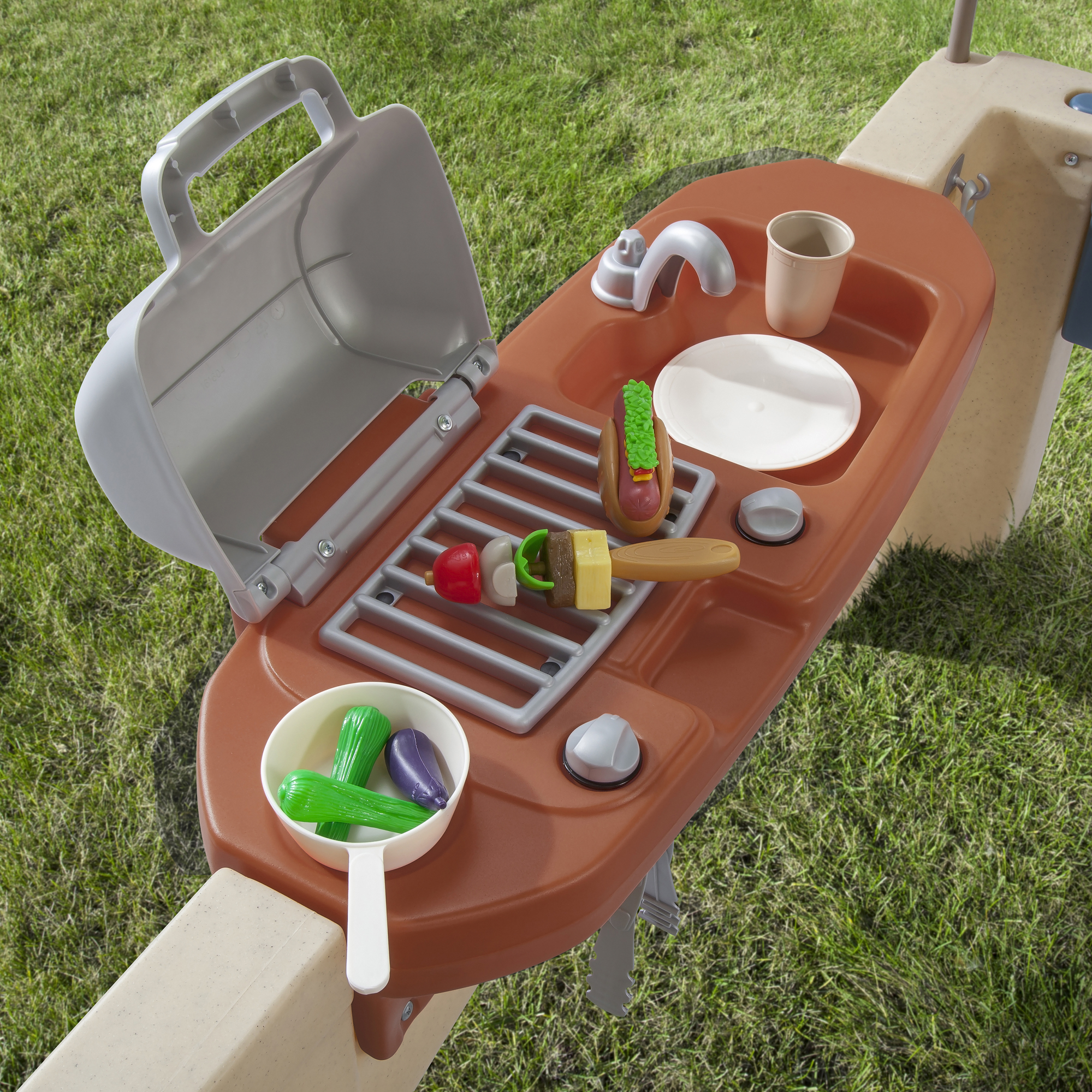 Spielzeug-Outdoorküche mit Grill, Spüle und Spielzeugessen auf Gras.