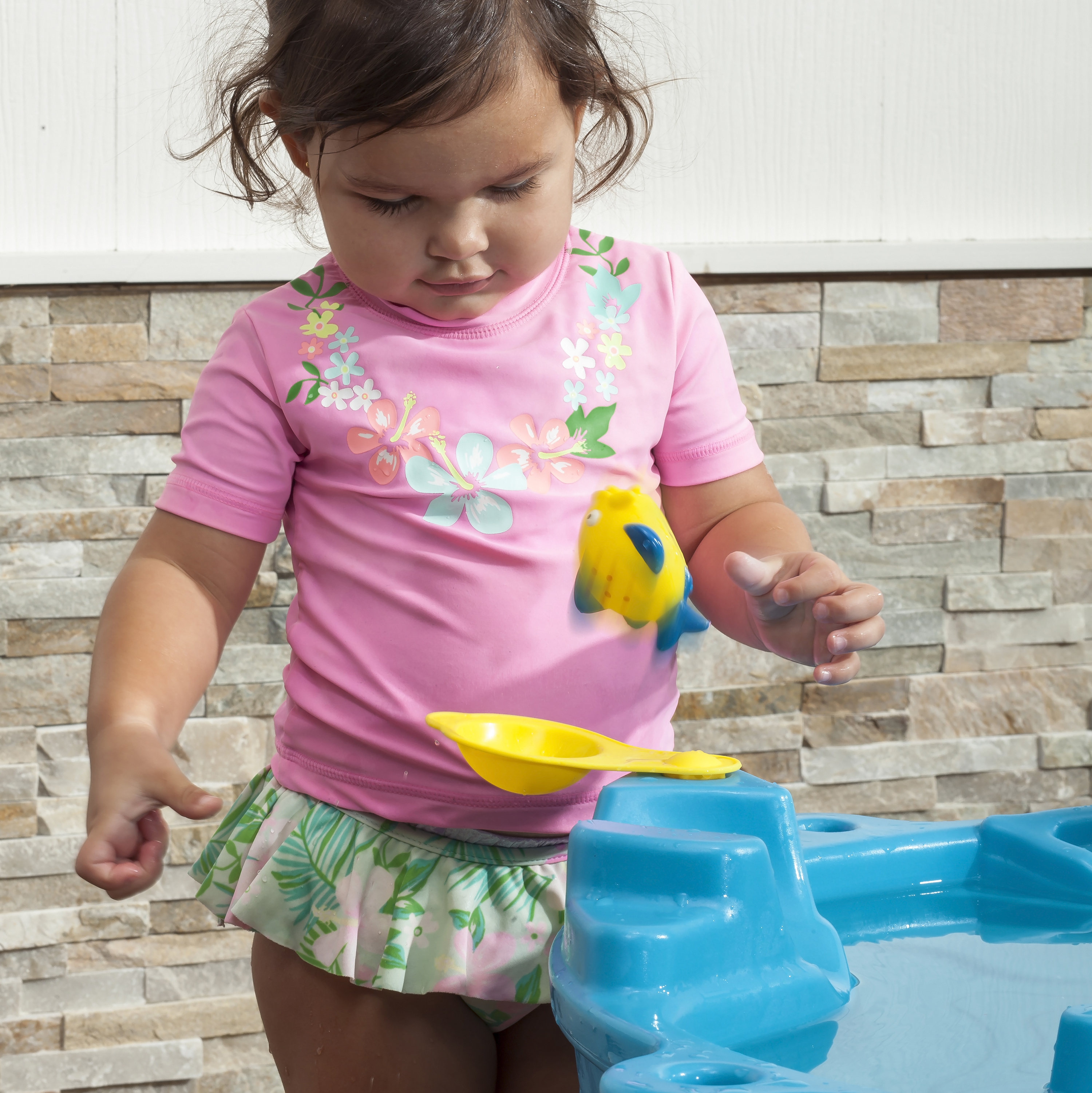 Ein junges Mädchen spielt mit einem gelben Spielzeugfisch und einem blauen Wasserspiel.