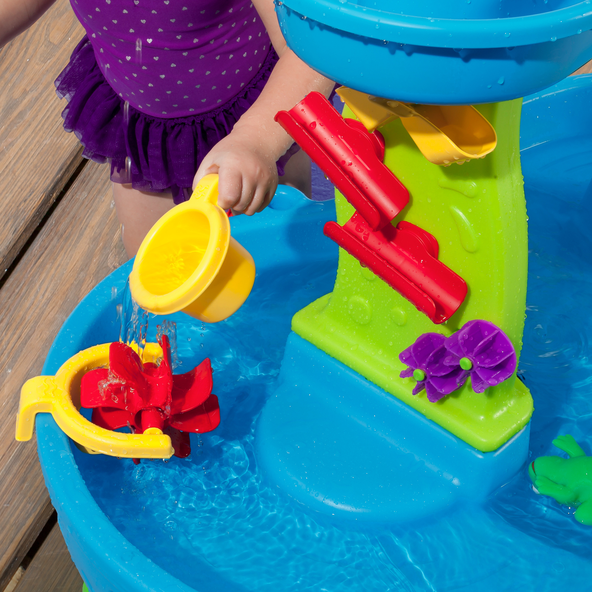 Kind spielt mit einem Wassertisch und gießt Wasser.