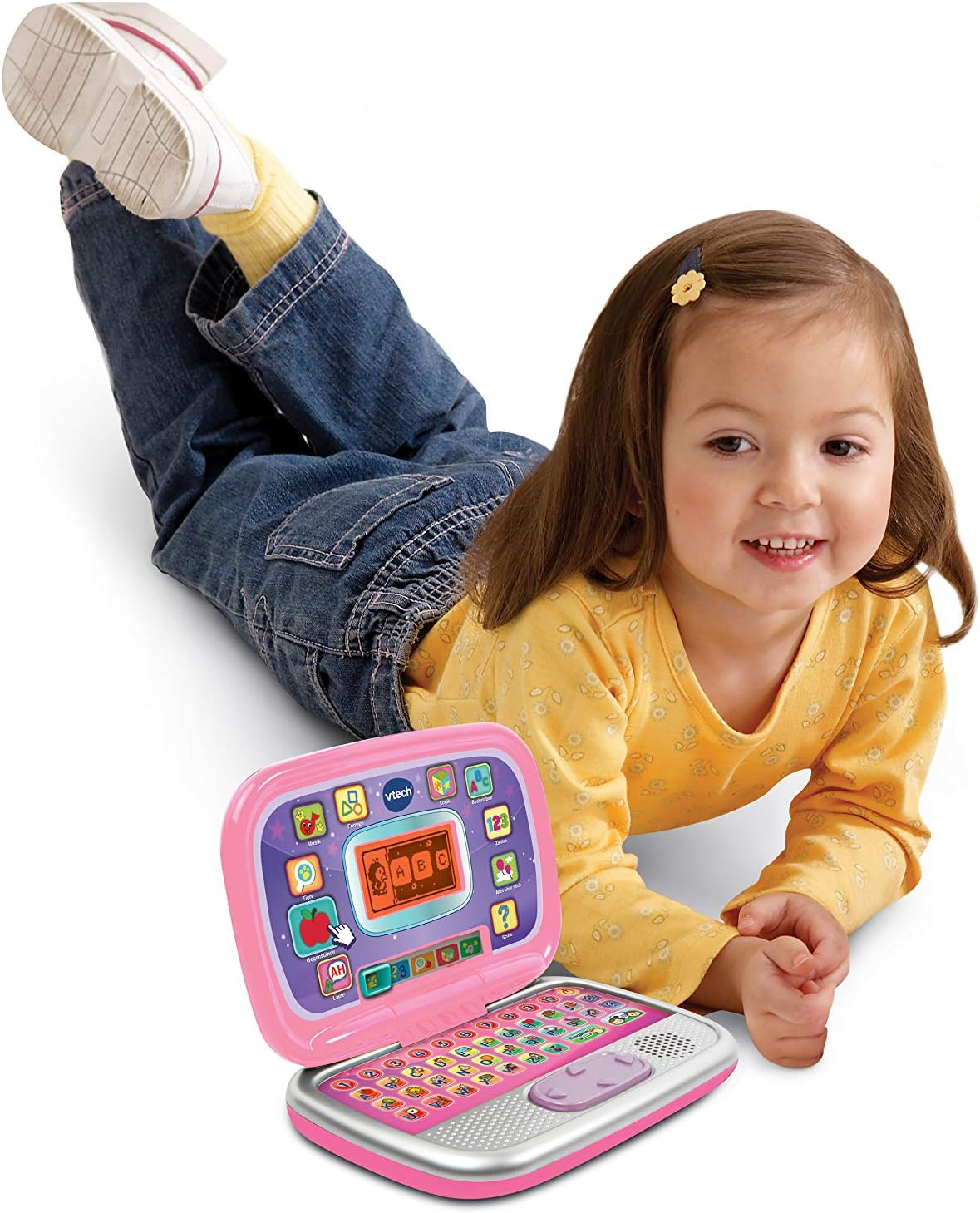 Junges Mädchen liegt neben einem rosa Spielzeug-Laptop und lächelt.