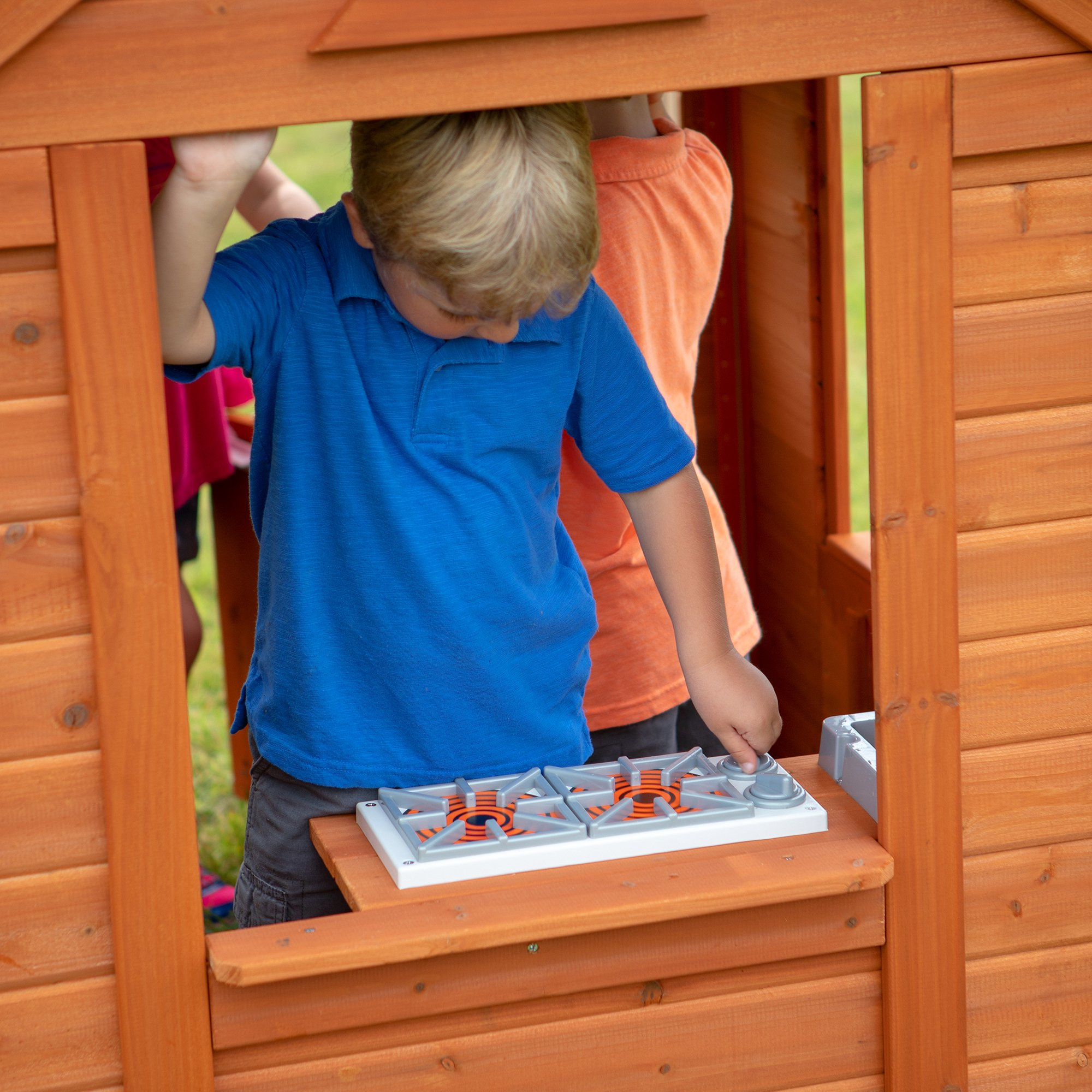 Zwei Kinder spielen mit einem Spielzeugherd. Der Herd befindet sich in einem Spielhaus aus Holz.