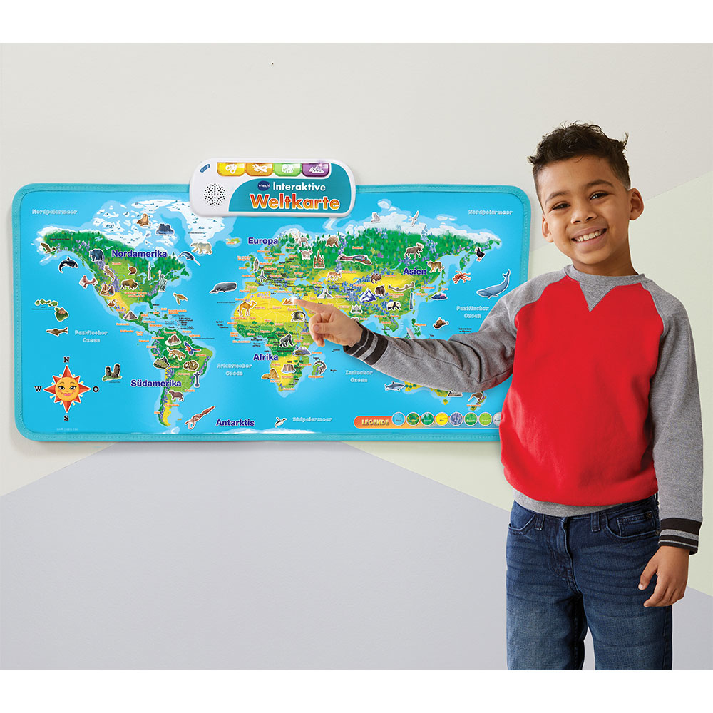 Ein Junge zeigt auf eine Weltkarte an der Wand. Die Karte ist blau mit beschrifteten Kontinenten.