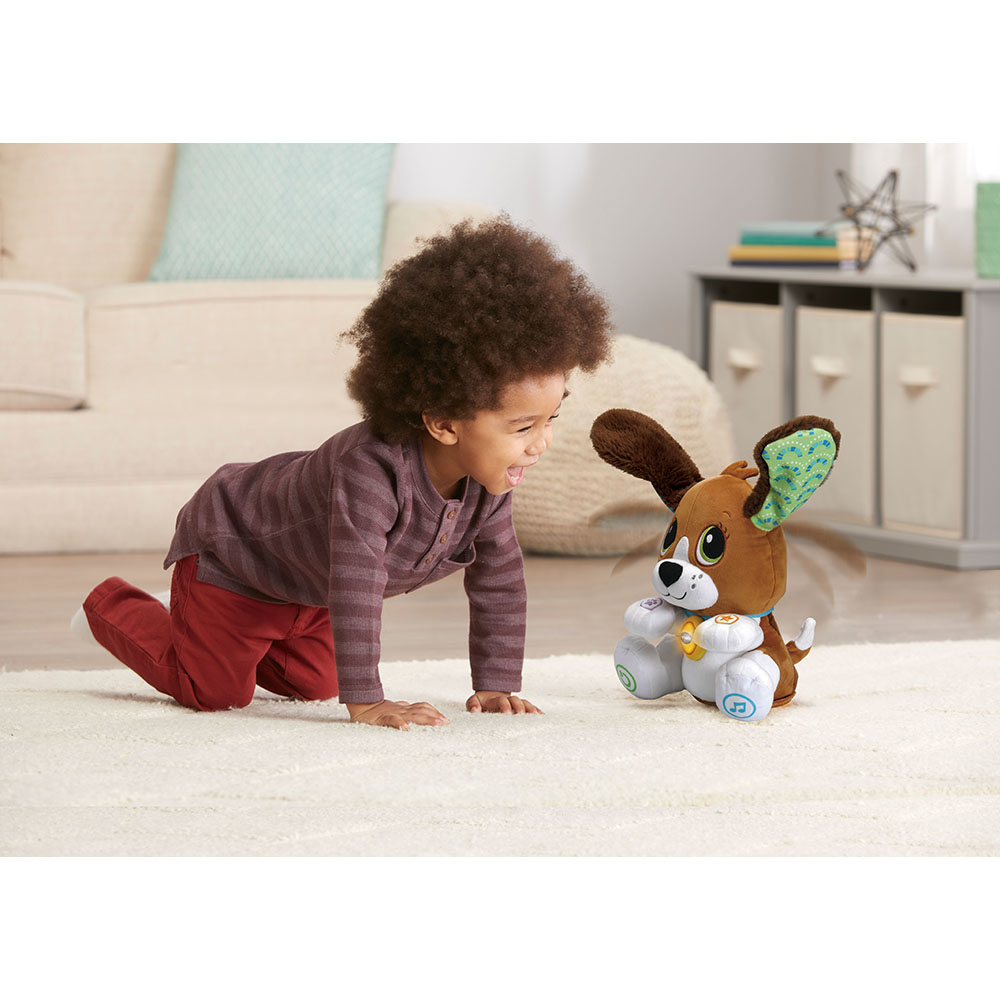 Ein Baby krabbelt auf einem weißen Teppich auf einen Spielzeughund zu, mit beigen Möbeln im Hintergrund.