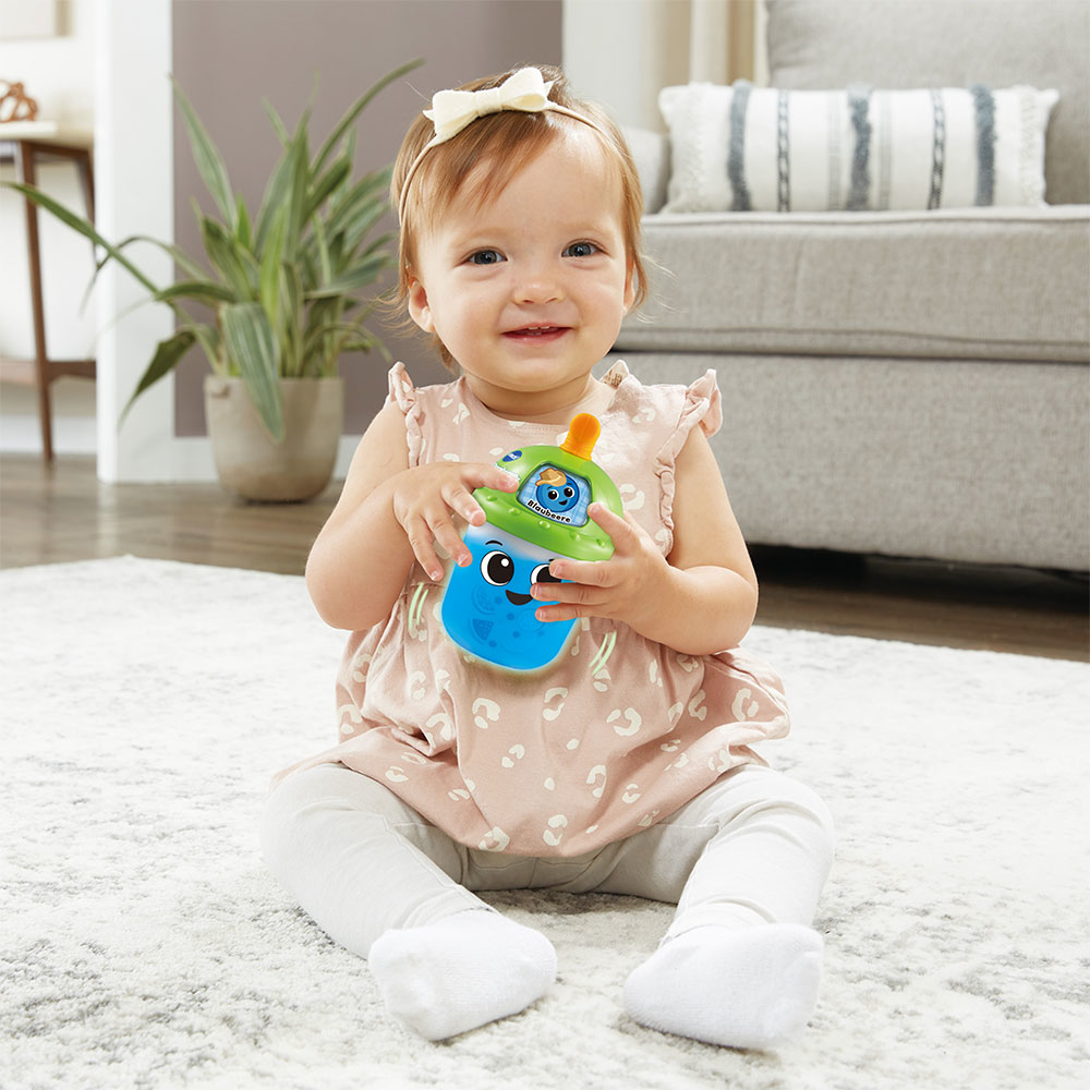 Baby hält einen blau-grünen Spielzeugbecher.