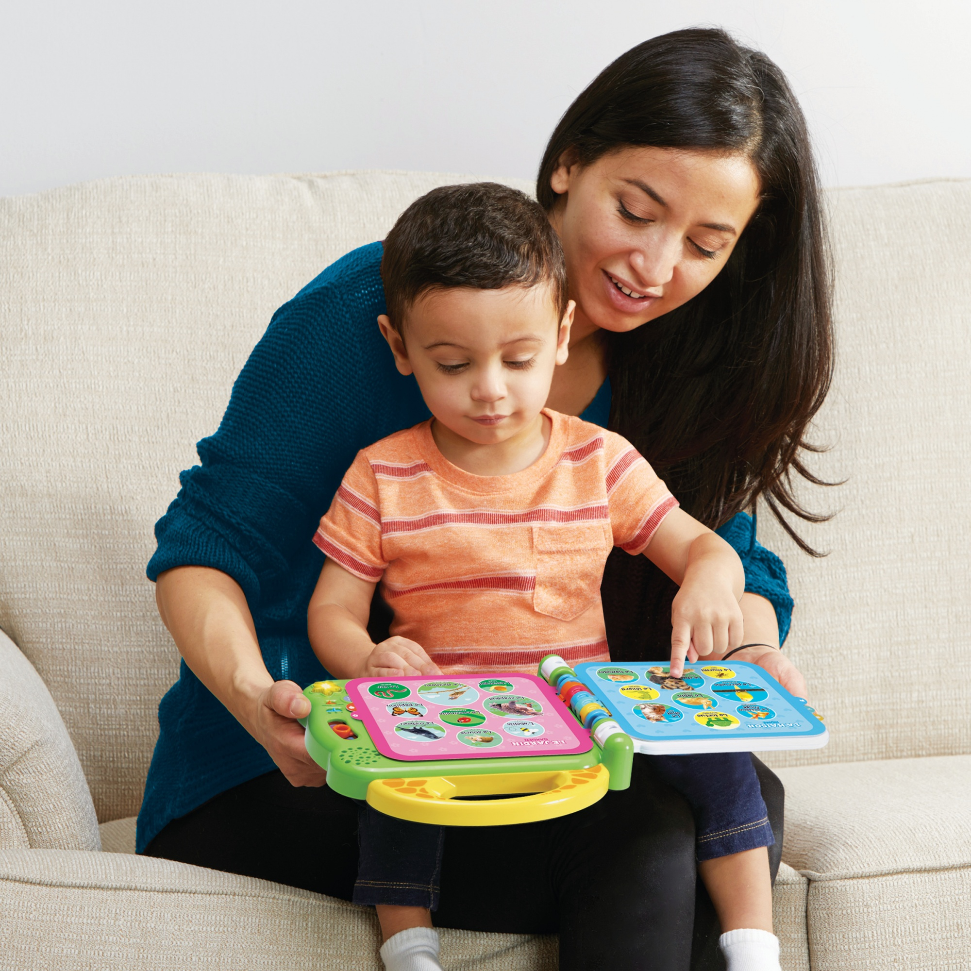 Una donna e un bambino seduti su un divano, che guardano un libro didattico per bambini colorato.