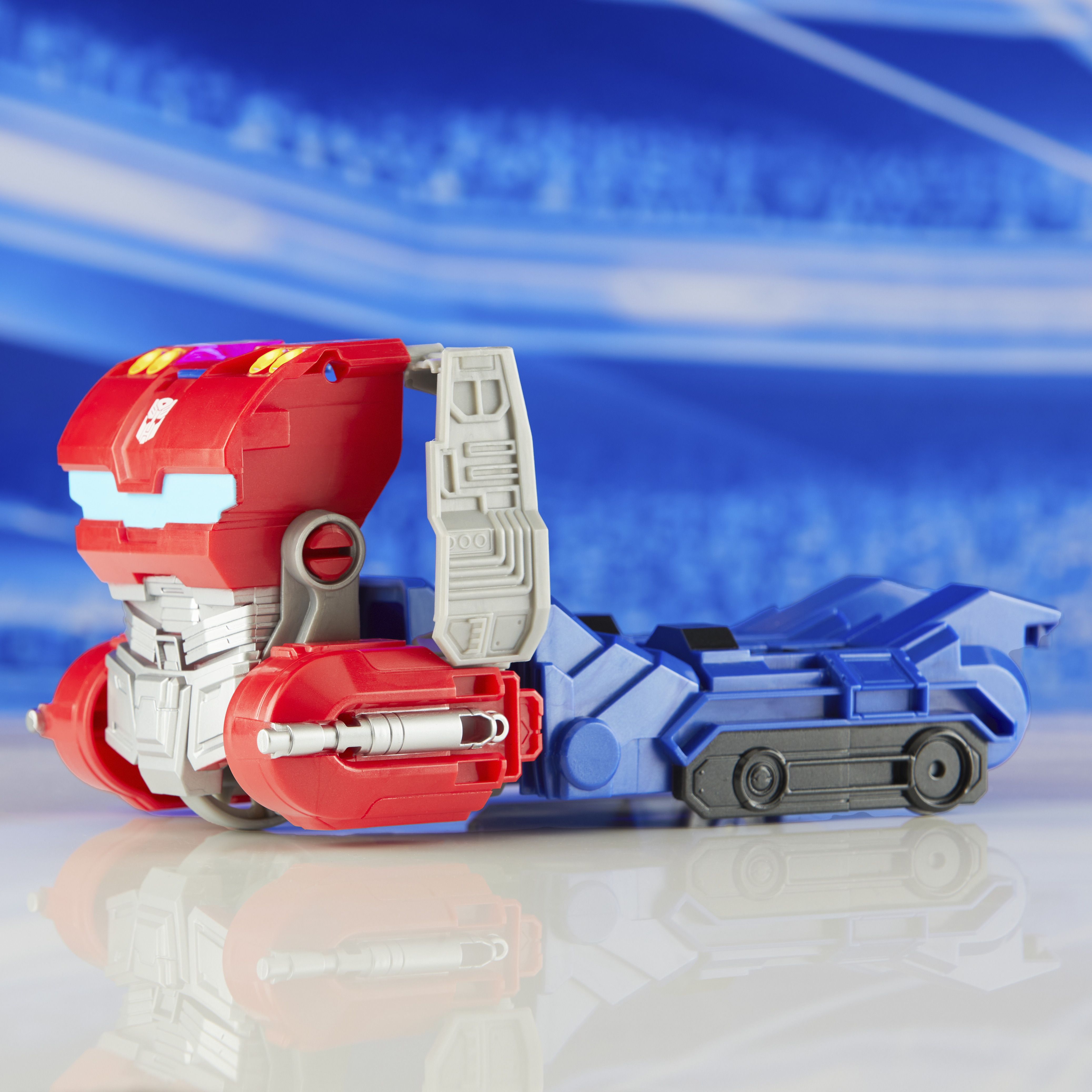 Un camion giocattolo rosso e blu su una superficie riflettente, contro uno sfondo blu sfocato.