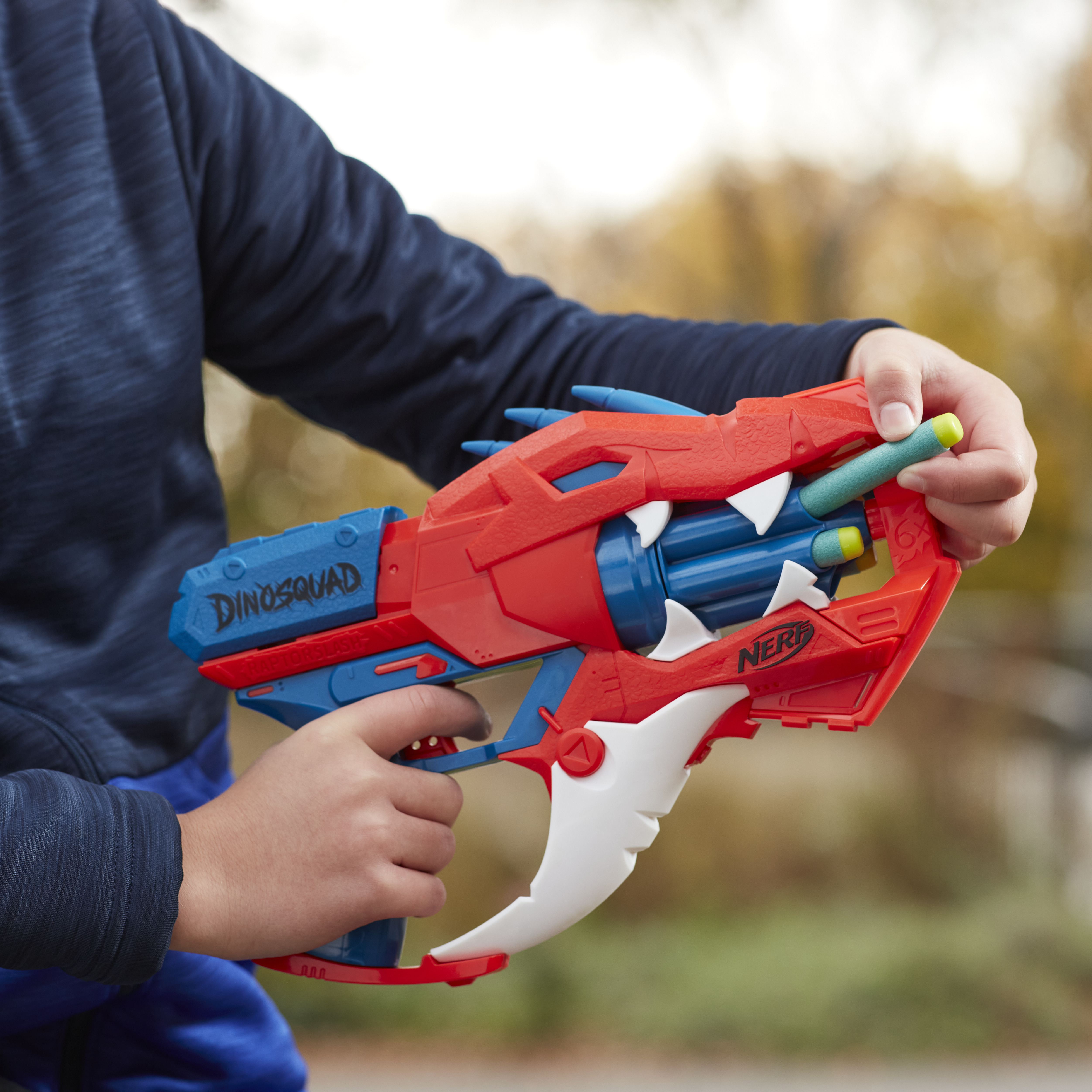 Dziecko trzymające zabawkę-pistolet. Czerwono-niebieski pistolet zabawkowy. Chłopiec w niebieskiej koszuli. Rozmyte tło.