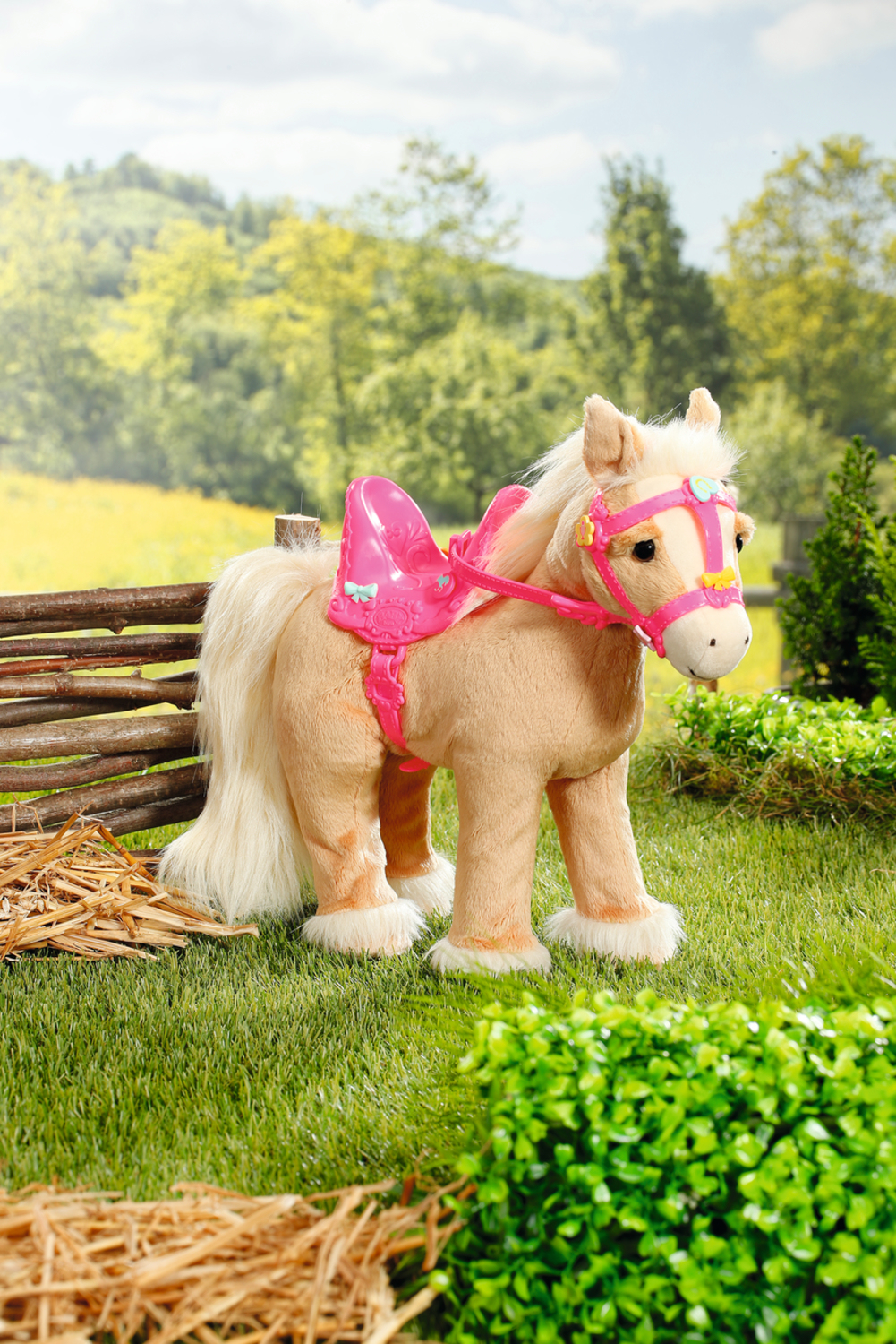 Ein Spielzeugpferd mit einem rosa Sattel und Zaumzeug steht auf Gras in der Nähe eines Zauns.