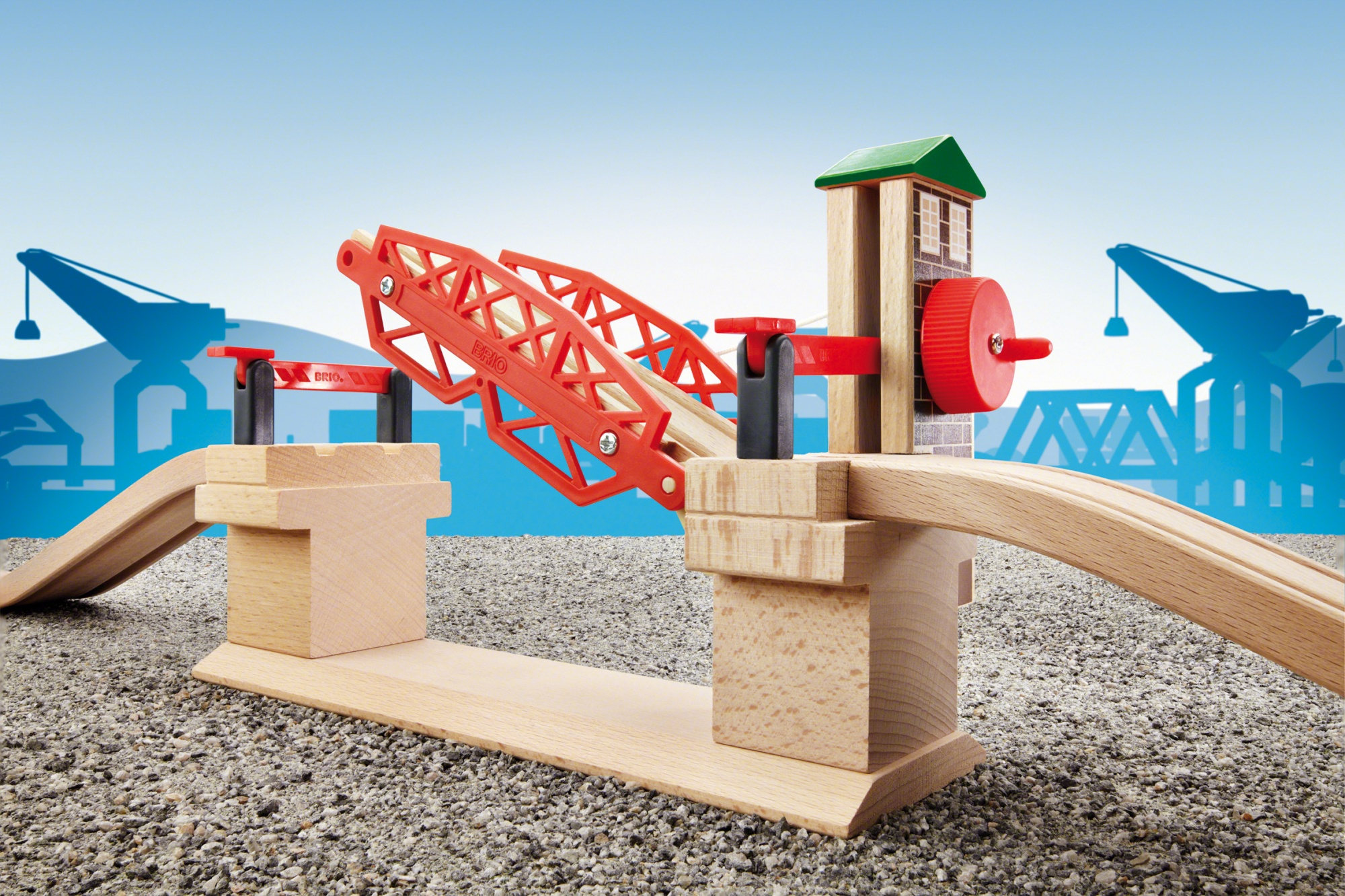 Eine Brio-Spielzeug-Hebebrücke mit roter Brücke und Holzkonstruktion mit blauem Himmel und Kränen im Hintergrund.