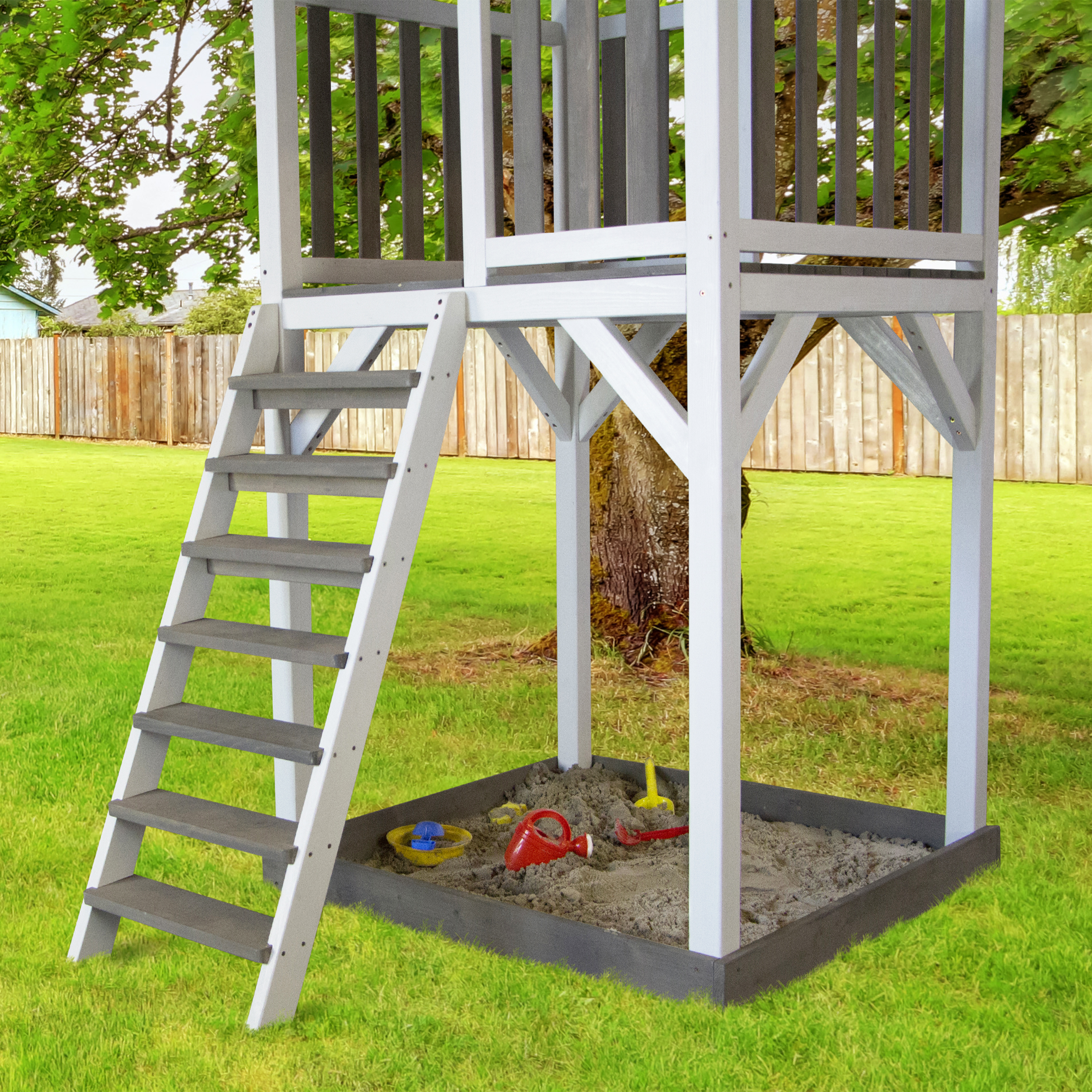 Spielplatz aus Holz mit Leiter, Stufen und Sandkasten. Es befindet sich in einem grasbewachsenen Garten mit Zaun.