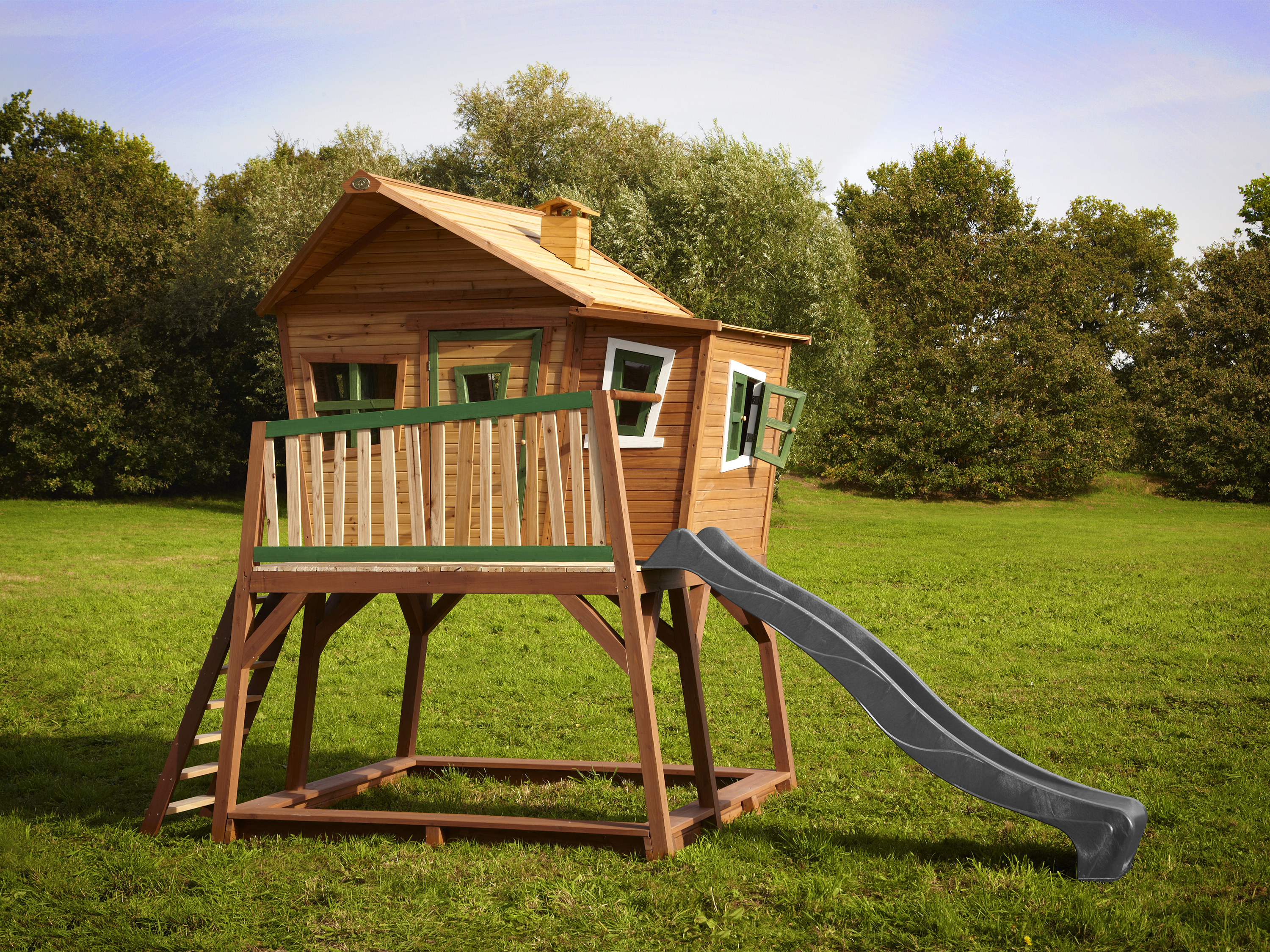 Ein Baumhaus aus Holz mit Rutsche und Leiter auf einer grünen Wiese.