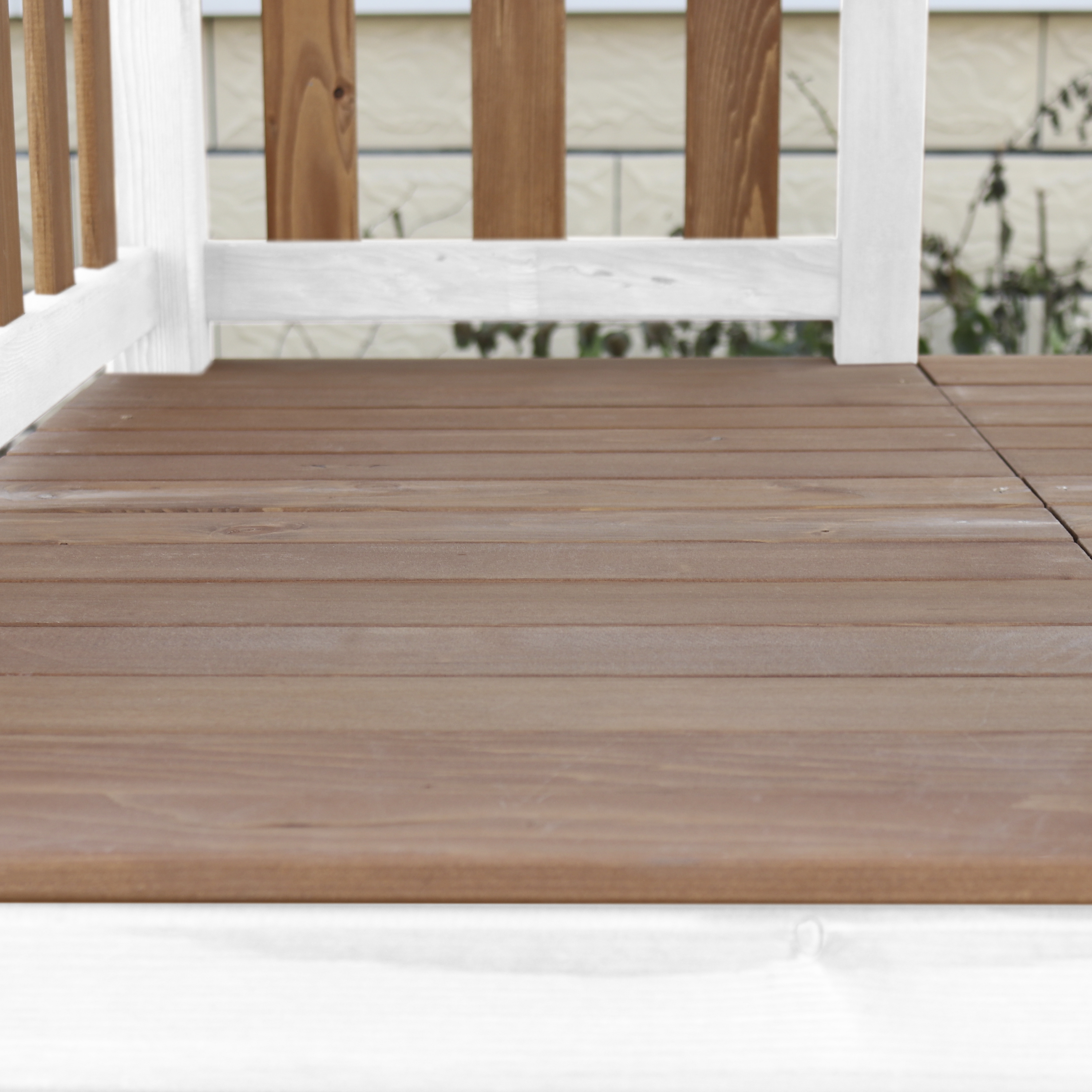 Holzdeck mit weißem Geländer, braunen Brettern und einem Blick auf eine Ziegelmauer.