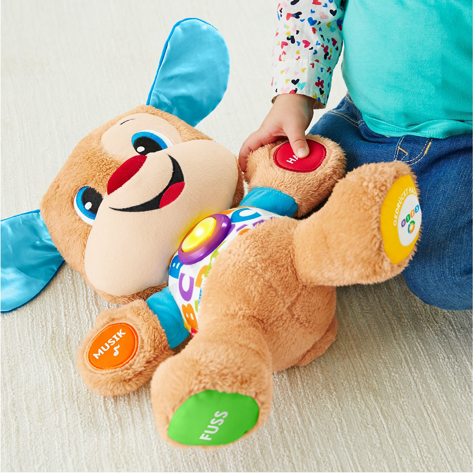 Ein Kind interagiert mit einem Plüschhundespielzeug und berührt die Knöpfe auf seinem Bauch.