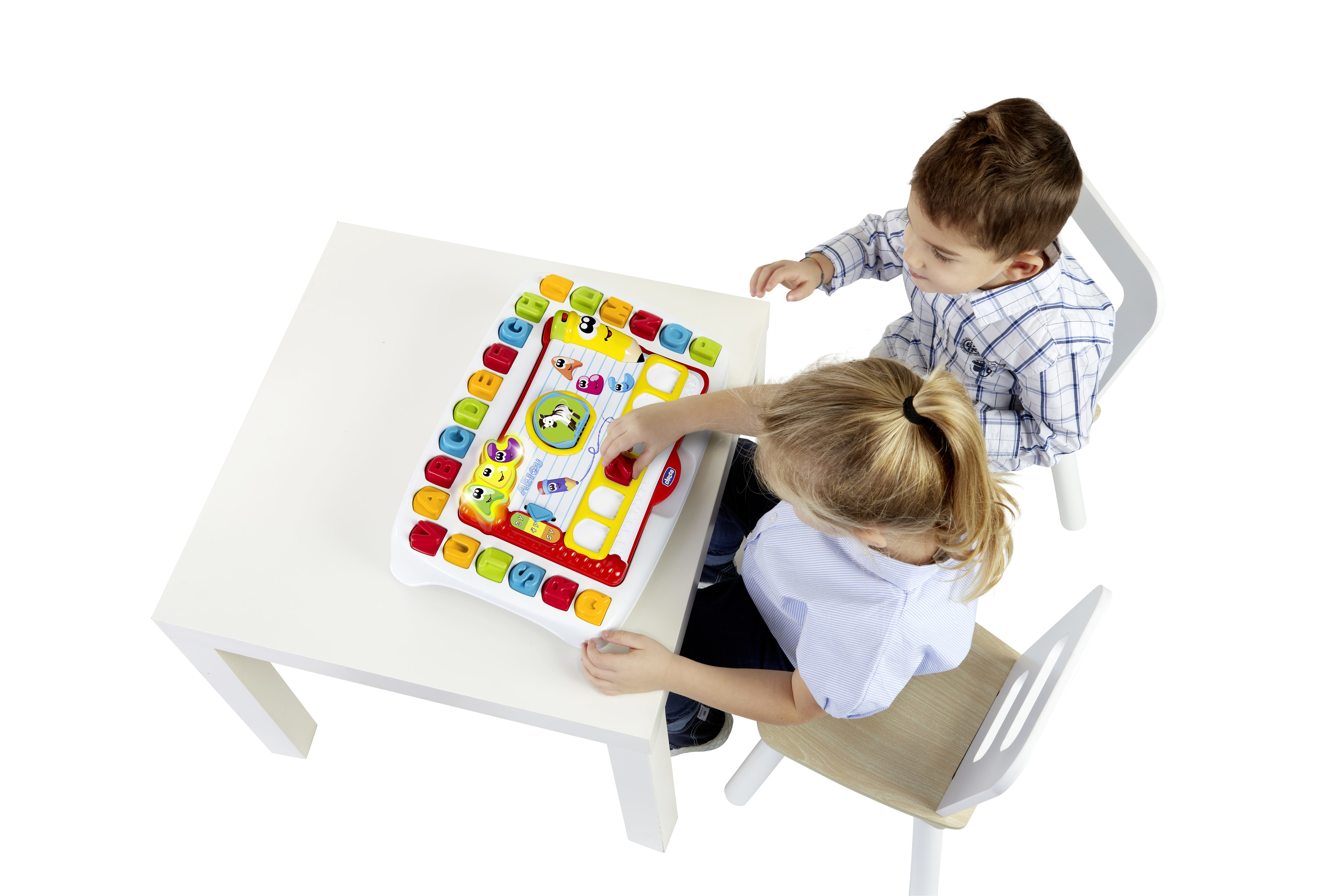Dwoje dzieci bawiących się kolorową elektroniczną zabawką edukacyjną na białym stole. Zabawka ma różne przyciski.