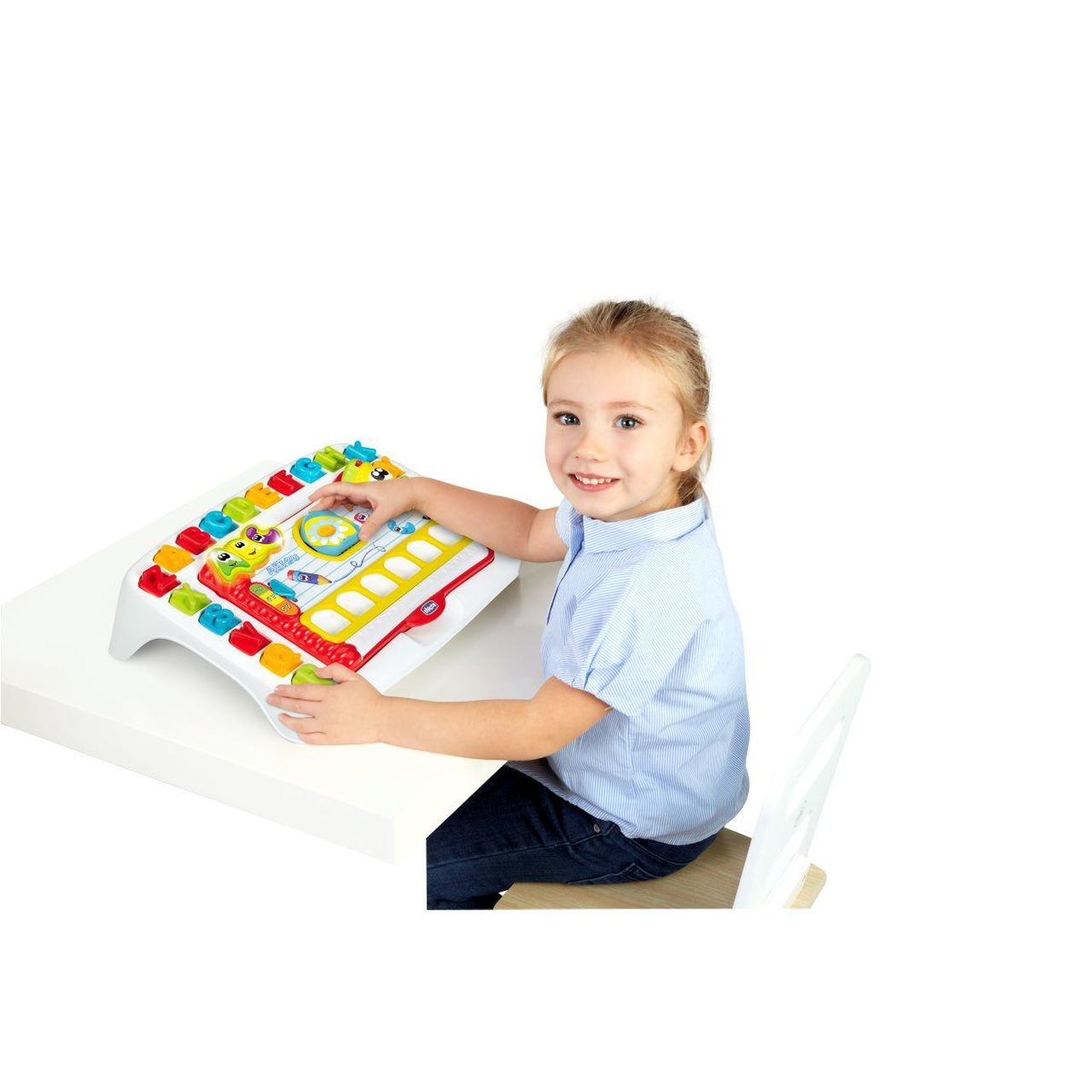 Mała dziewczynka siedzi przy stole i bawi się kolorową zabawką, uśmiechając się do kamery.