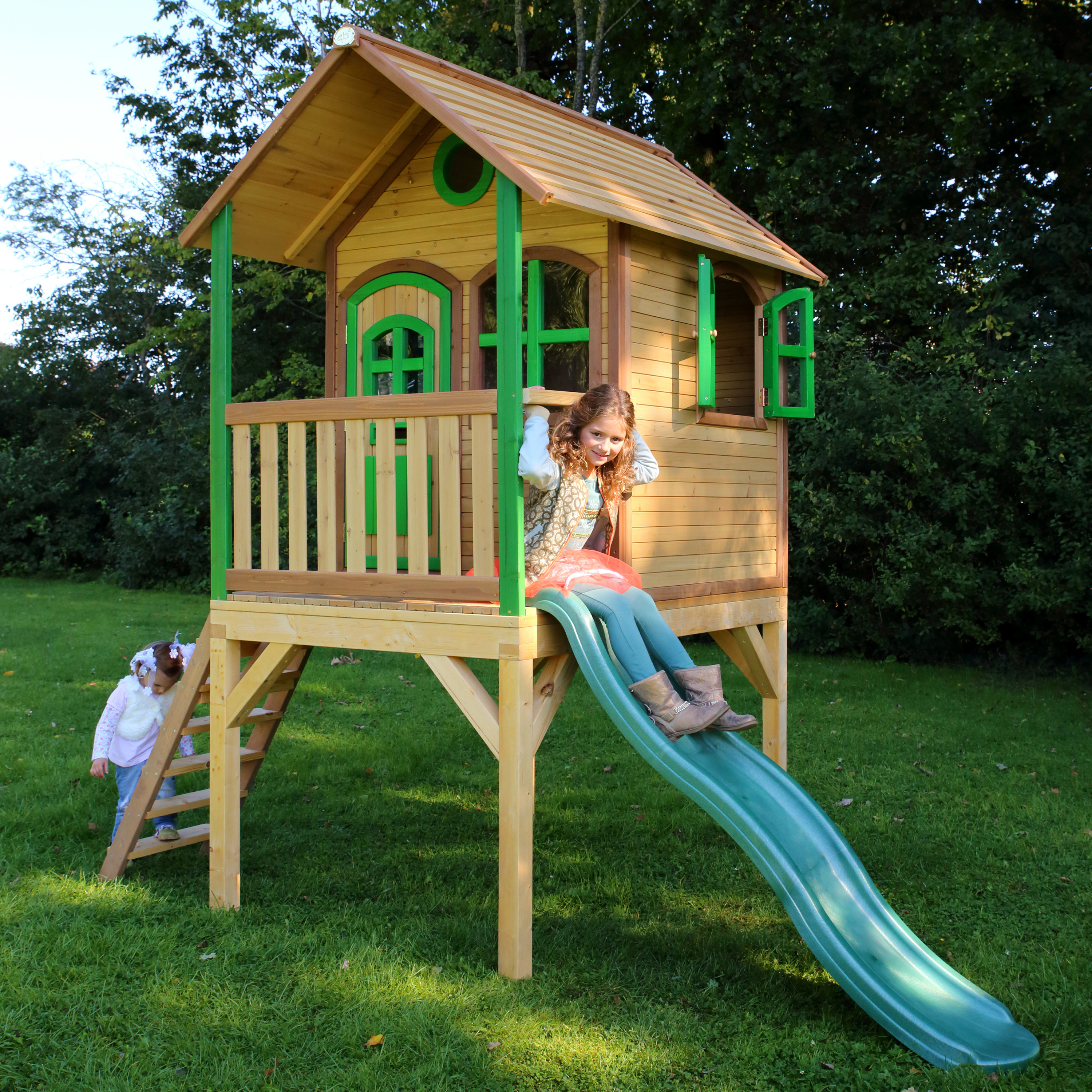 Kinder spielen in einem Spielhaus aus Holz. Grüne Rutsche, Holzstruktur. Sonniger Tag.