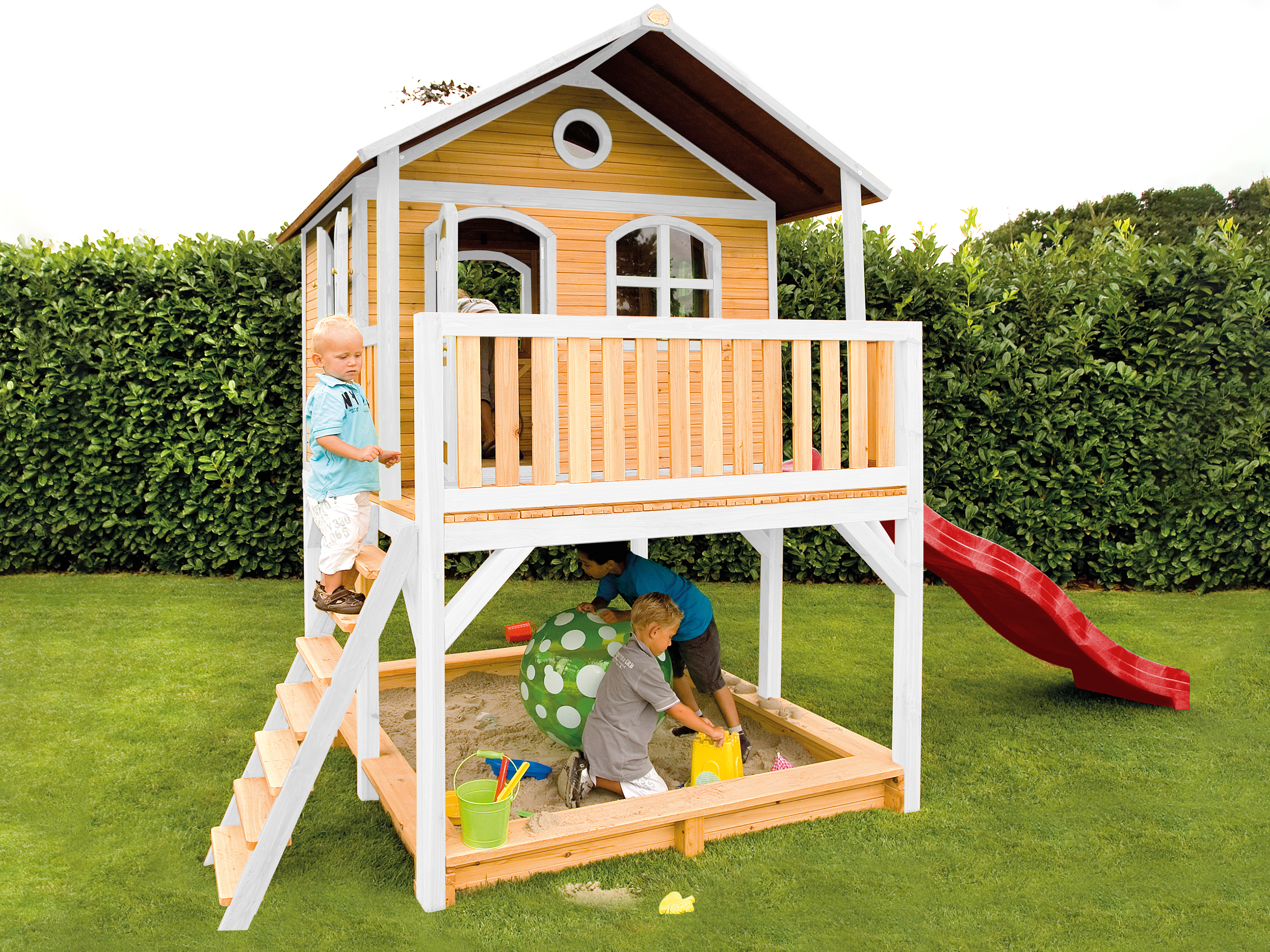 Spielhaus mit Rutsche, Treppe und Sandkasten. Zwei Kinder spielen im Sandkasten.