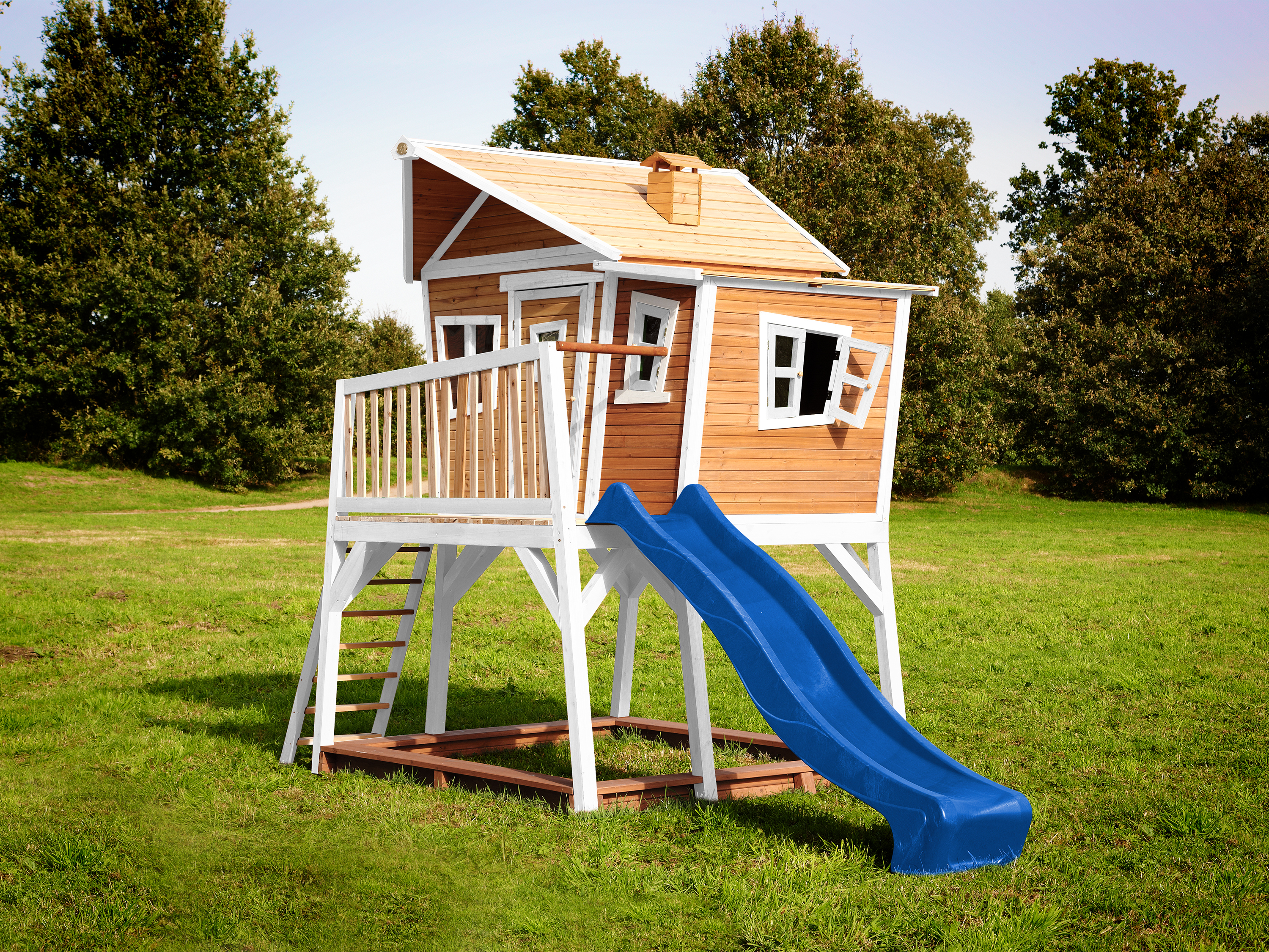 Ein hölzernes Spielset mit Haus, Rutsche und Bäumen im Hintergrund.