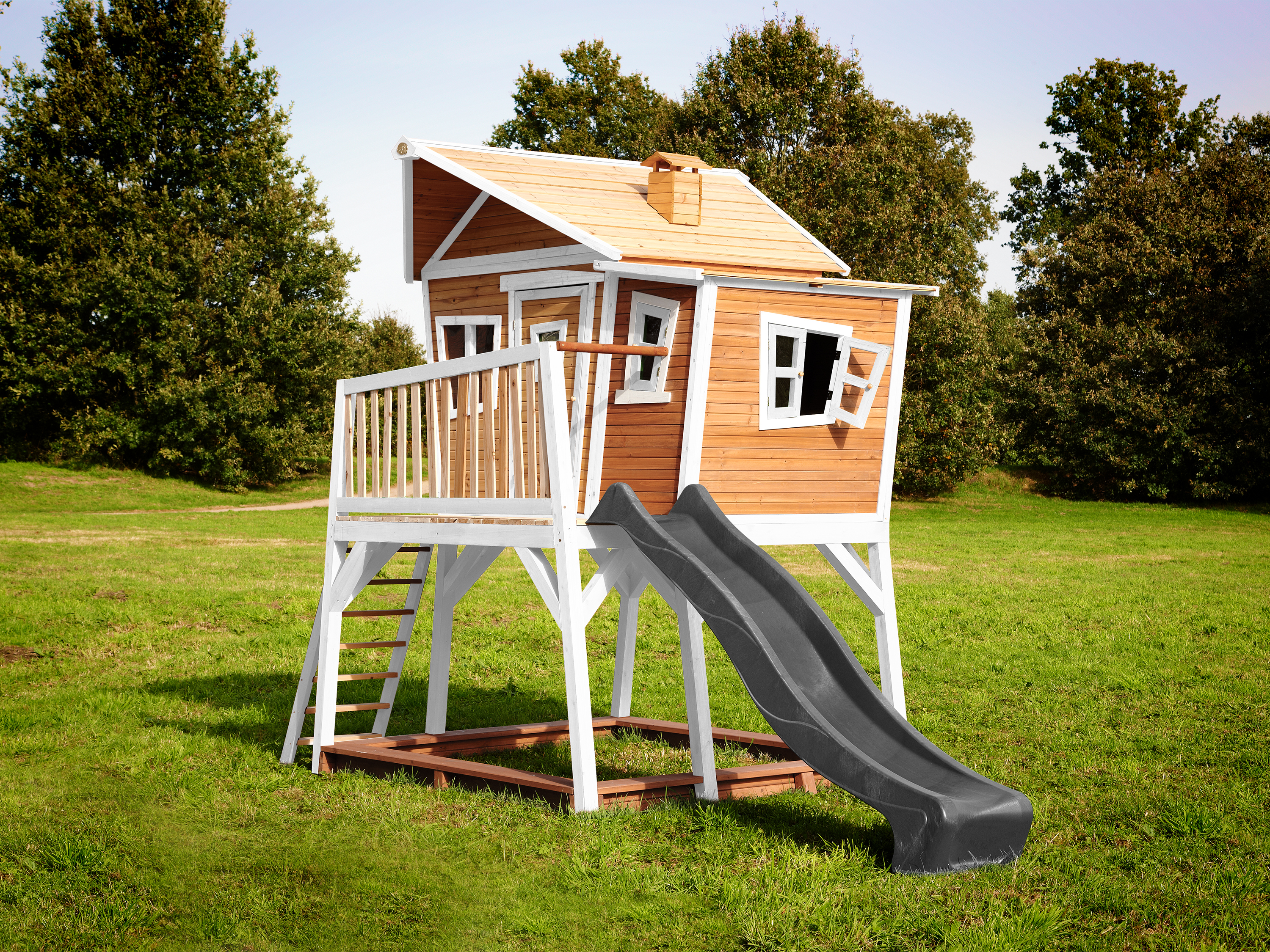 Ein hölzernes Spielhaus mit Rutsche, Leiter und spielenden Kindern auf einer Rasenfläche.