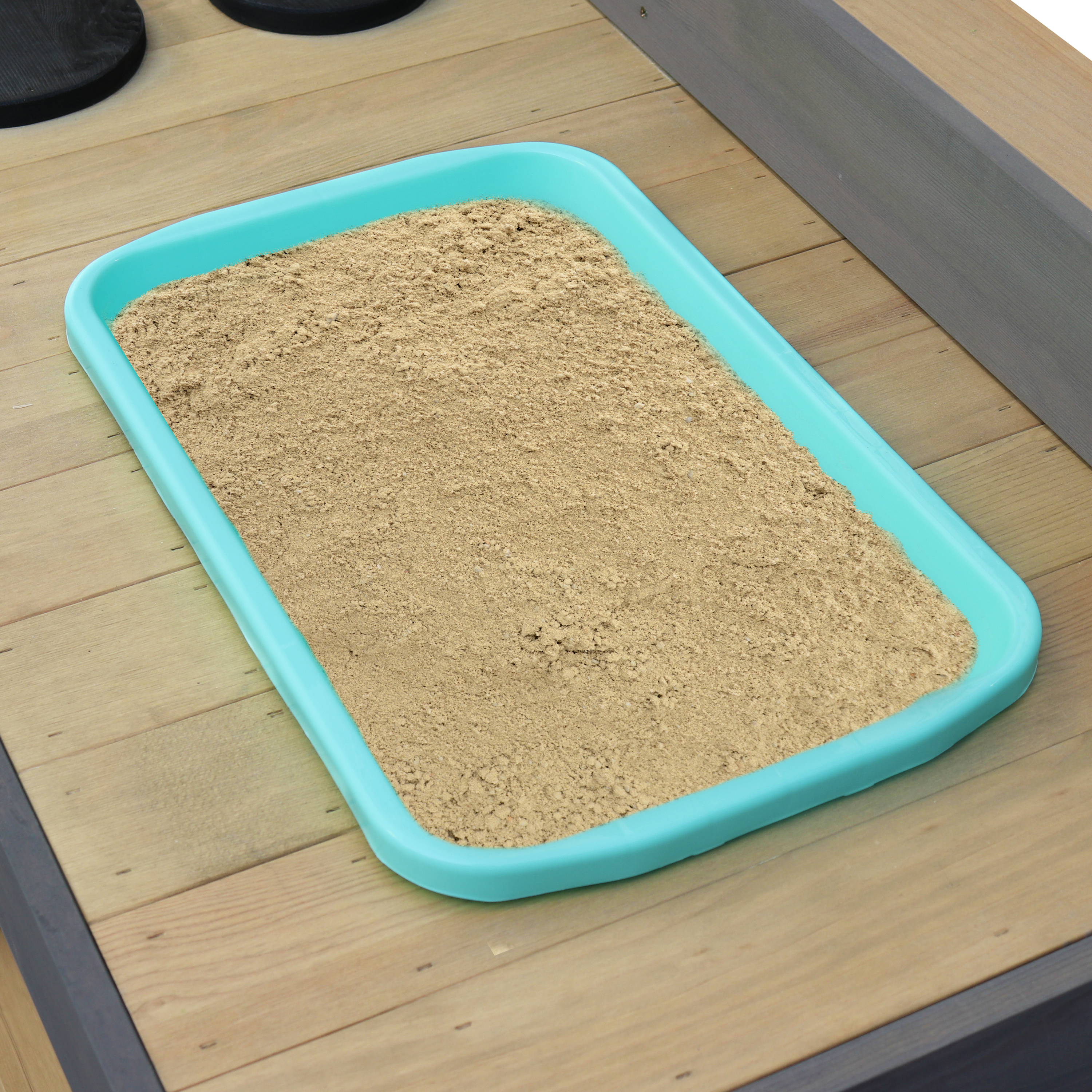 Eine türkisfarbene Sandkastenschale gefüllt mit Sand, platziert auf Holzplanken. Sand ist hellbraun.