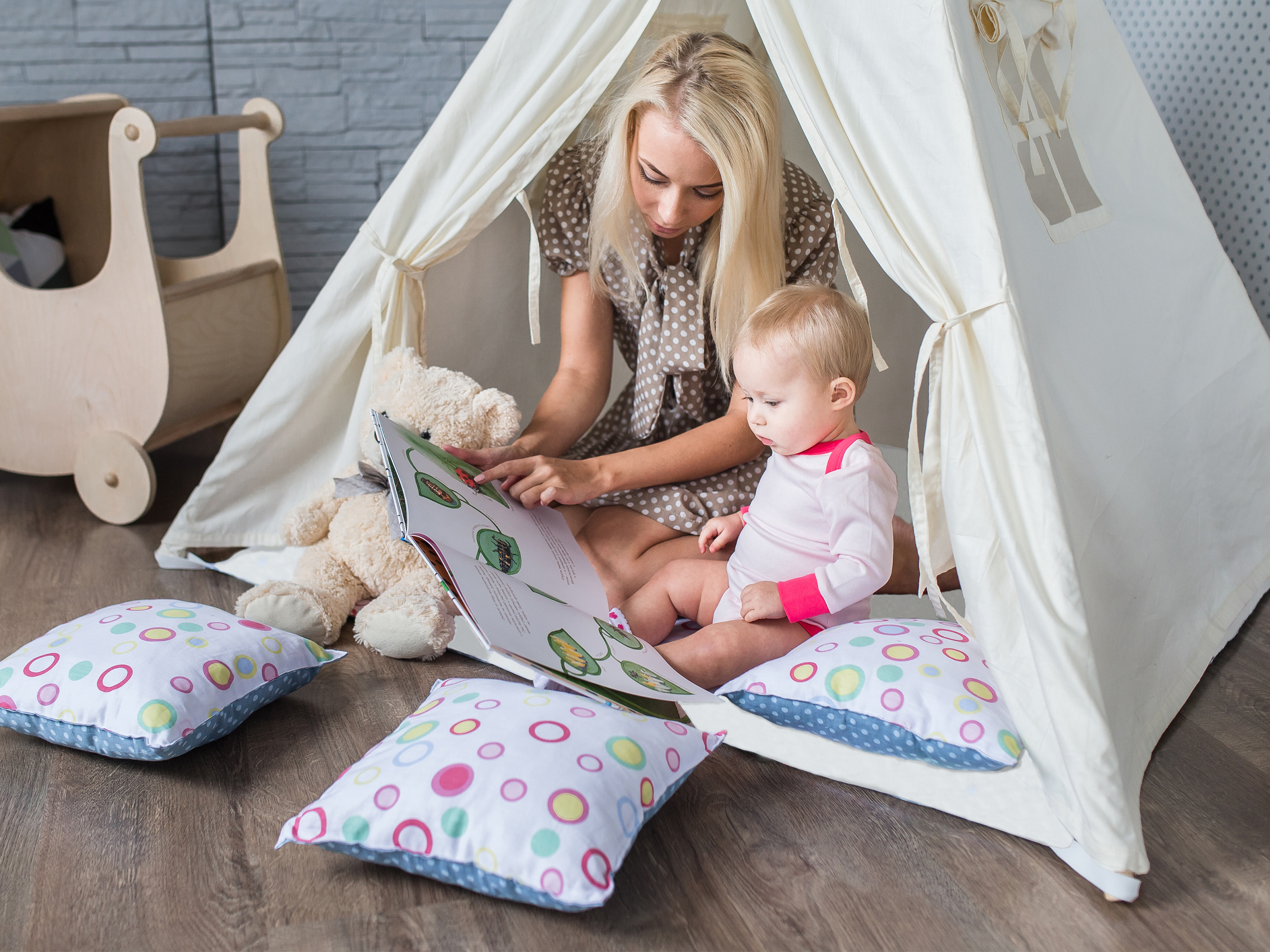 Eine Frau liest einem Baby in einem Zelt vor. Kissen und ein Spielzeugwagen sind in der Nähe.