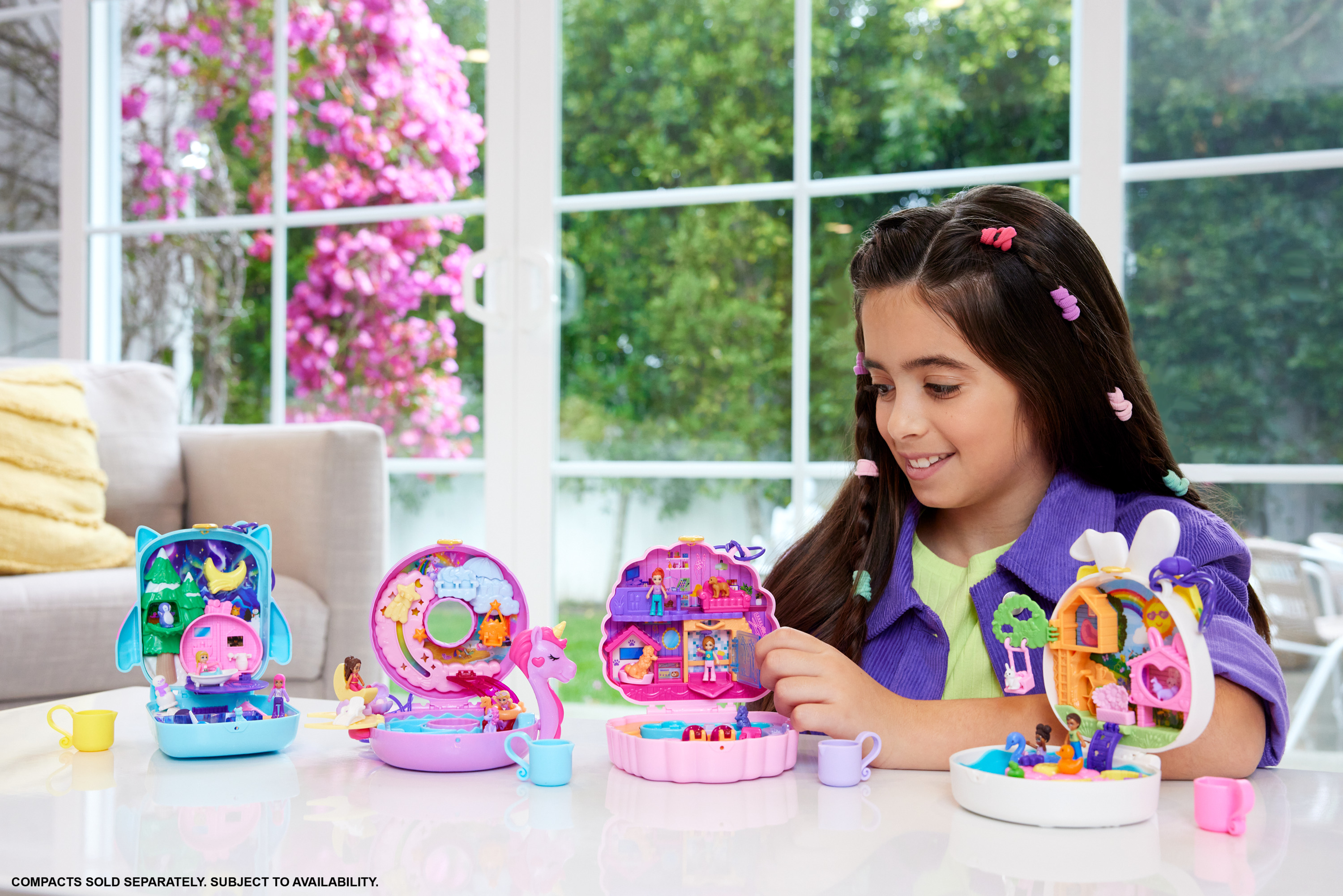 Niña sonriendo ante varios sets de Polly Pocket sobre una mesa blanca.