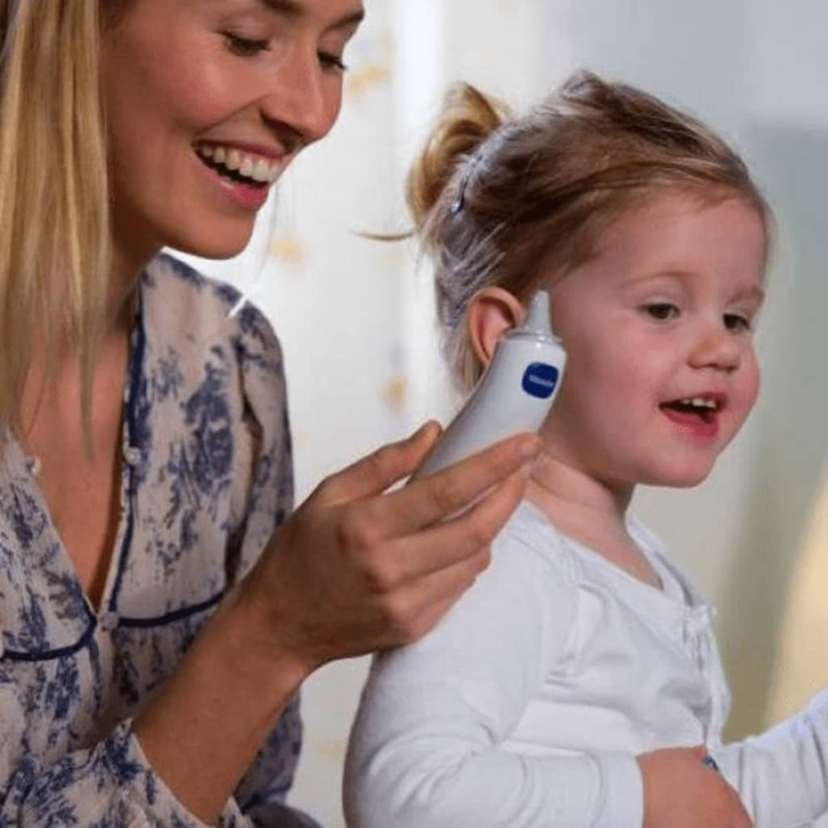 Kobieta sprawdza temperaturę dziecka termometrem do ucha. Oboje się uśmiechają.