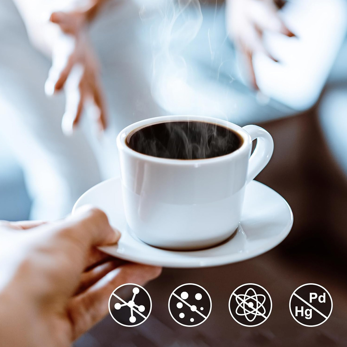Eine Hand, die eine weiße Tasse Kaffee mit aufsteigendem Dampf anbietet. Darunter Symbole für keine Schadstoffe.