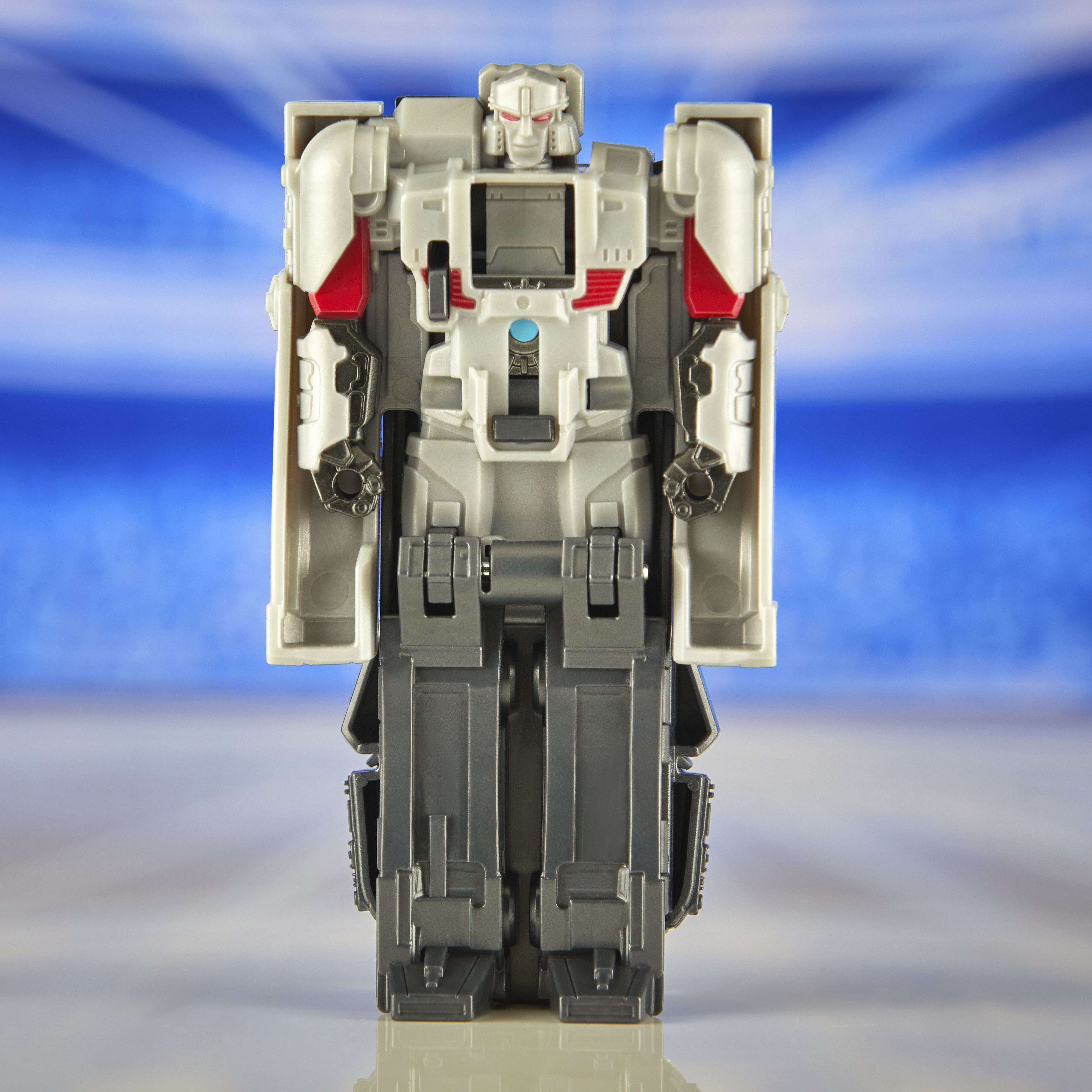 Juguete robot gris y blanco, vista frontal, con fondo borroso azul y blanco.