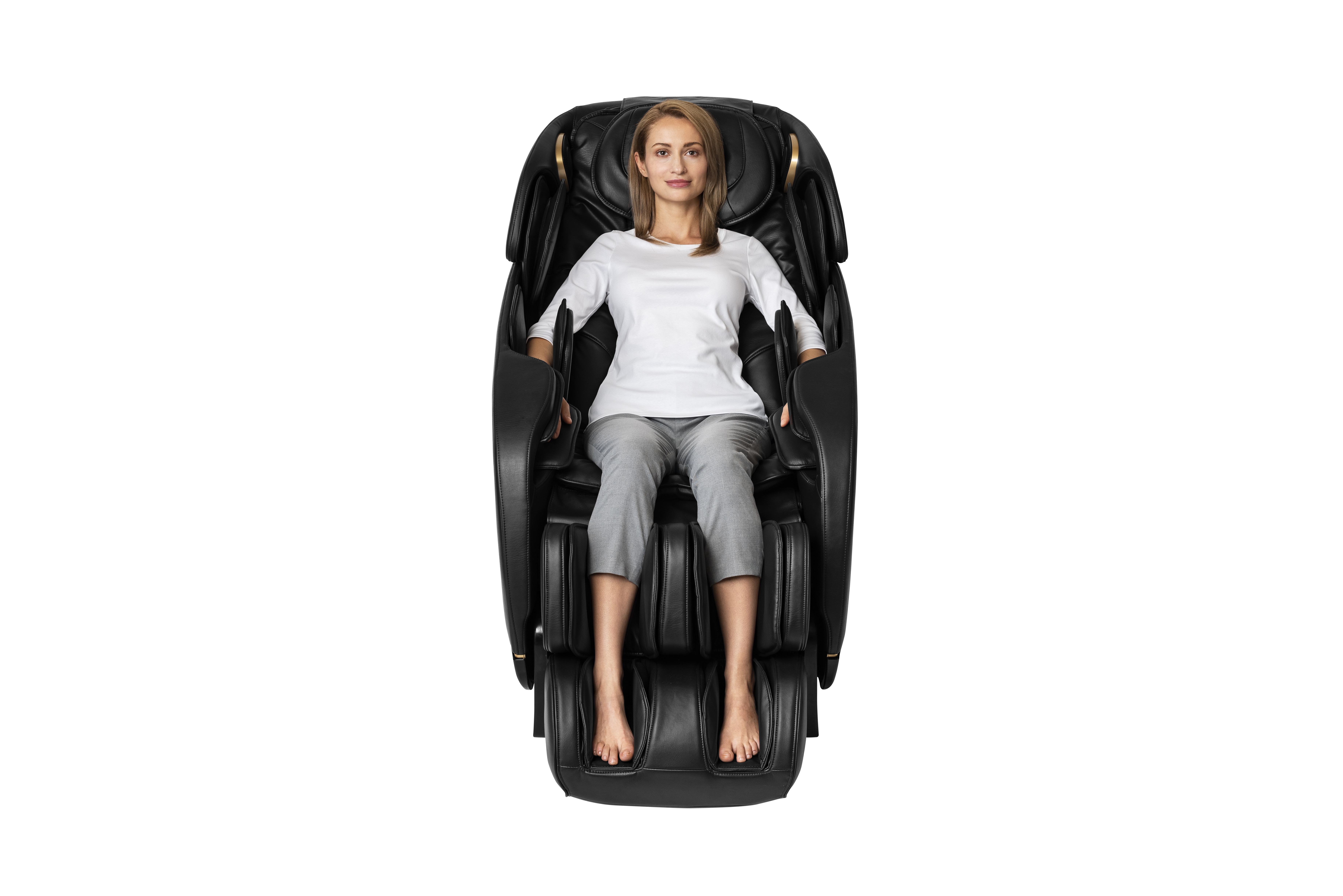 A woman sitting in a black massage chair, white shirt and gray pants, on a white background.