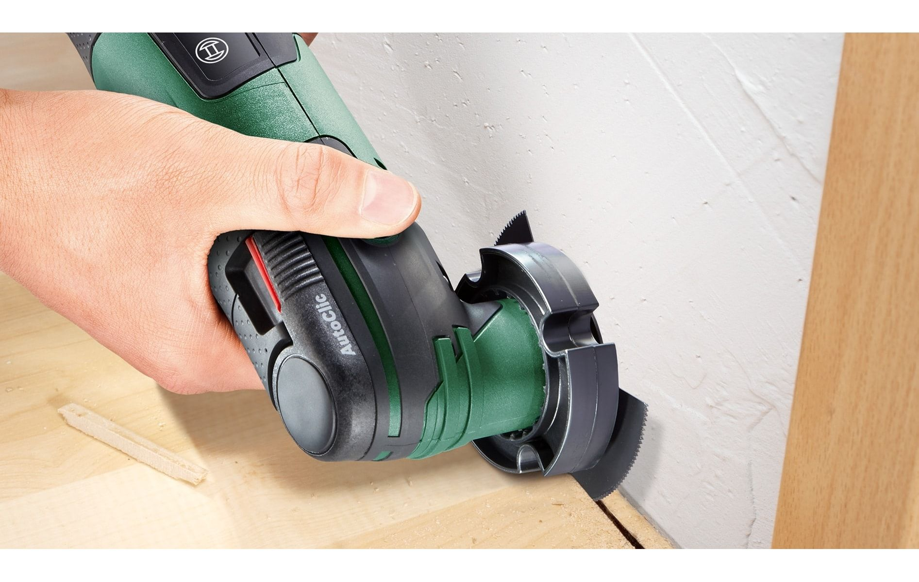 Hand, die ein Multitool verwendet, um Holz in der Nähe eines Holzbodens und einer Wand zu schneiden.