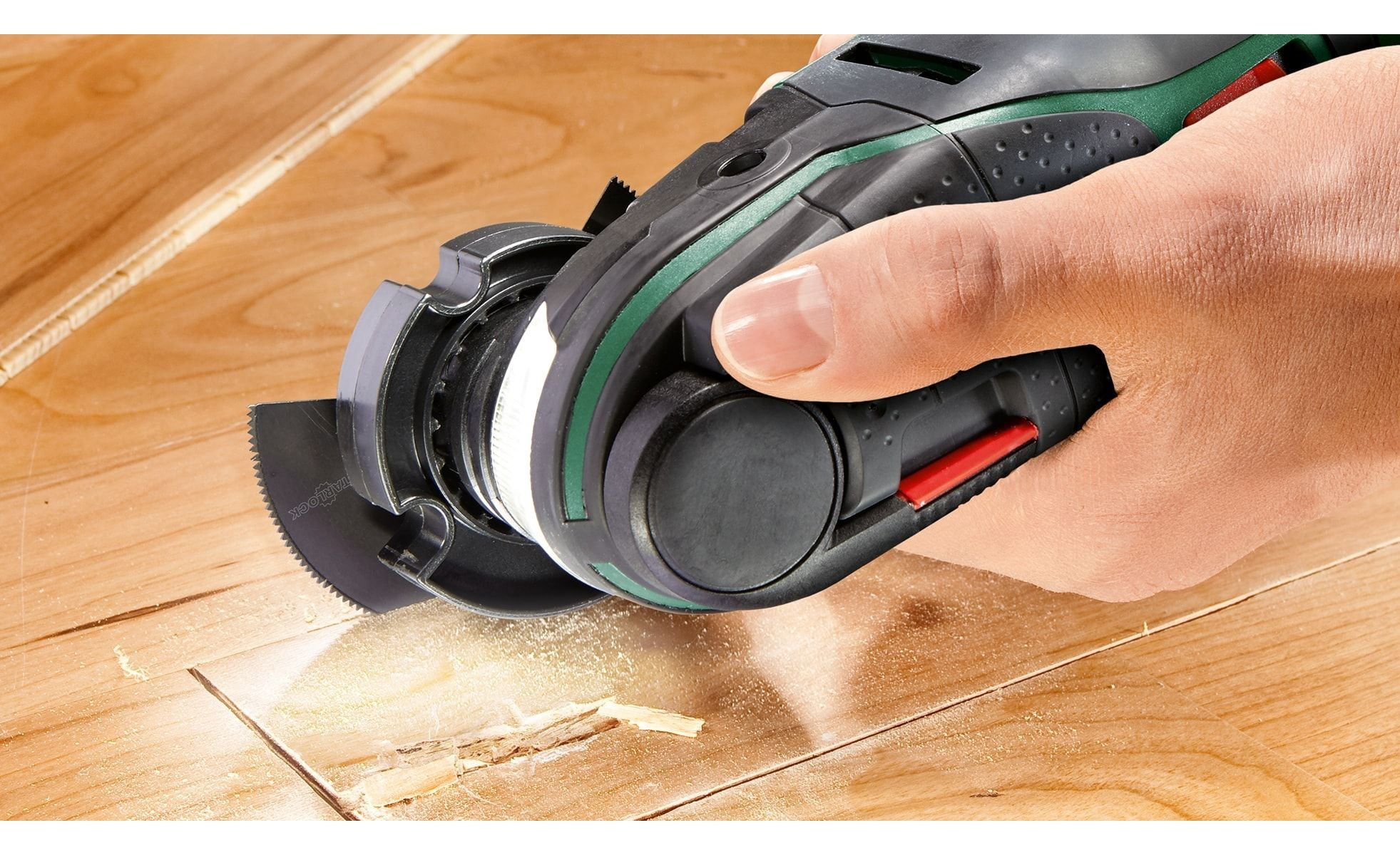 Die Hand einer Person, die ein Multitool verwendet, um einen Holzboden zu schneiden. Sägemehl ist sichtbar.
