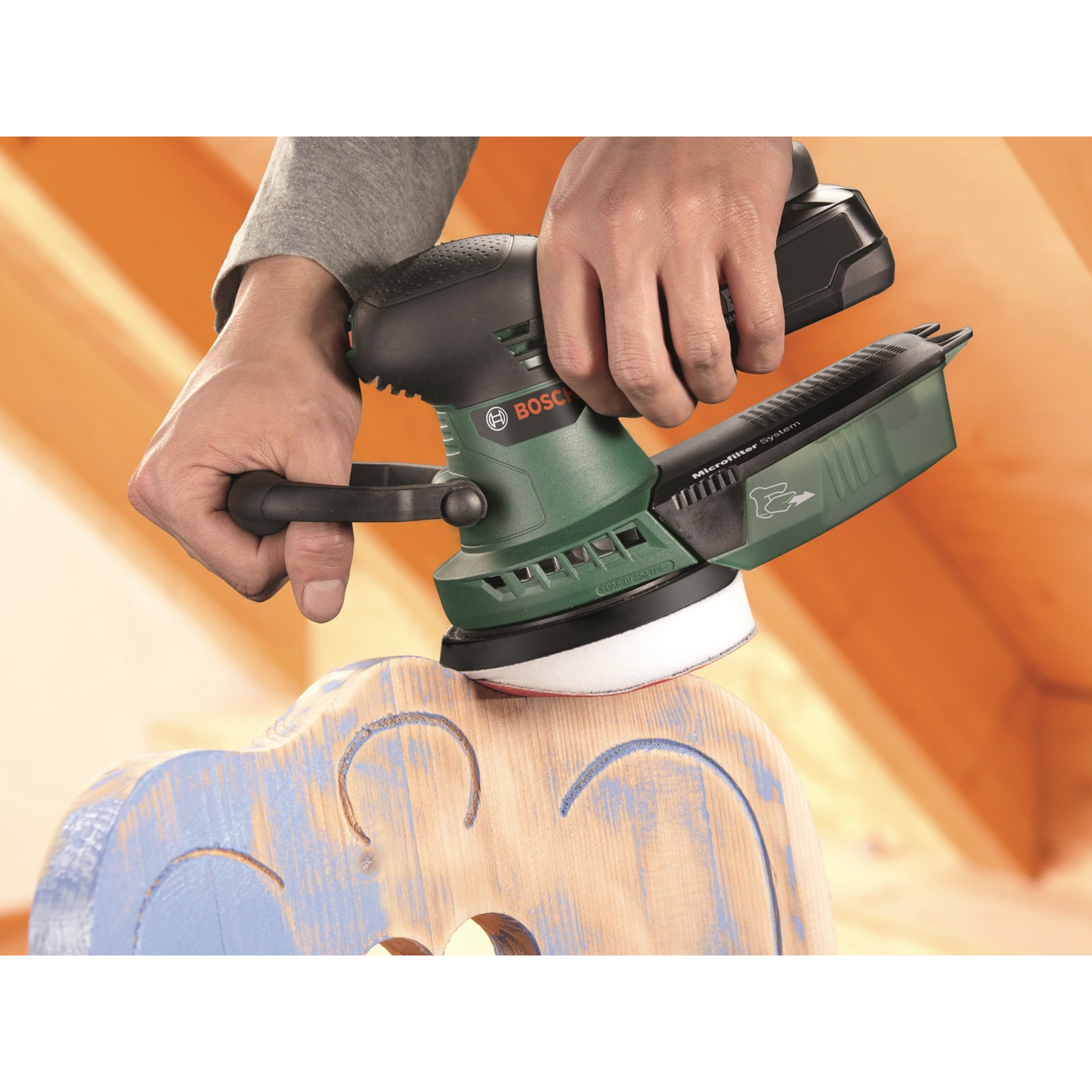 Une personne utilise une ponceuse Bosch verte et noire sur une chaise en bois.