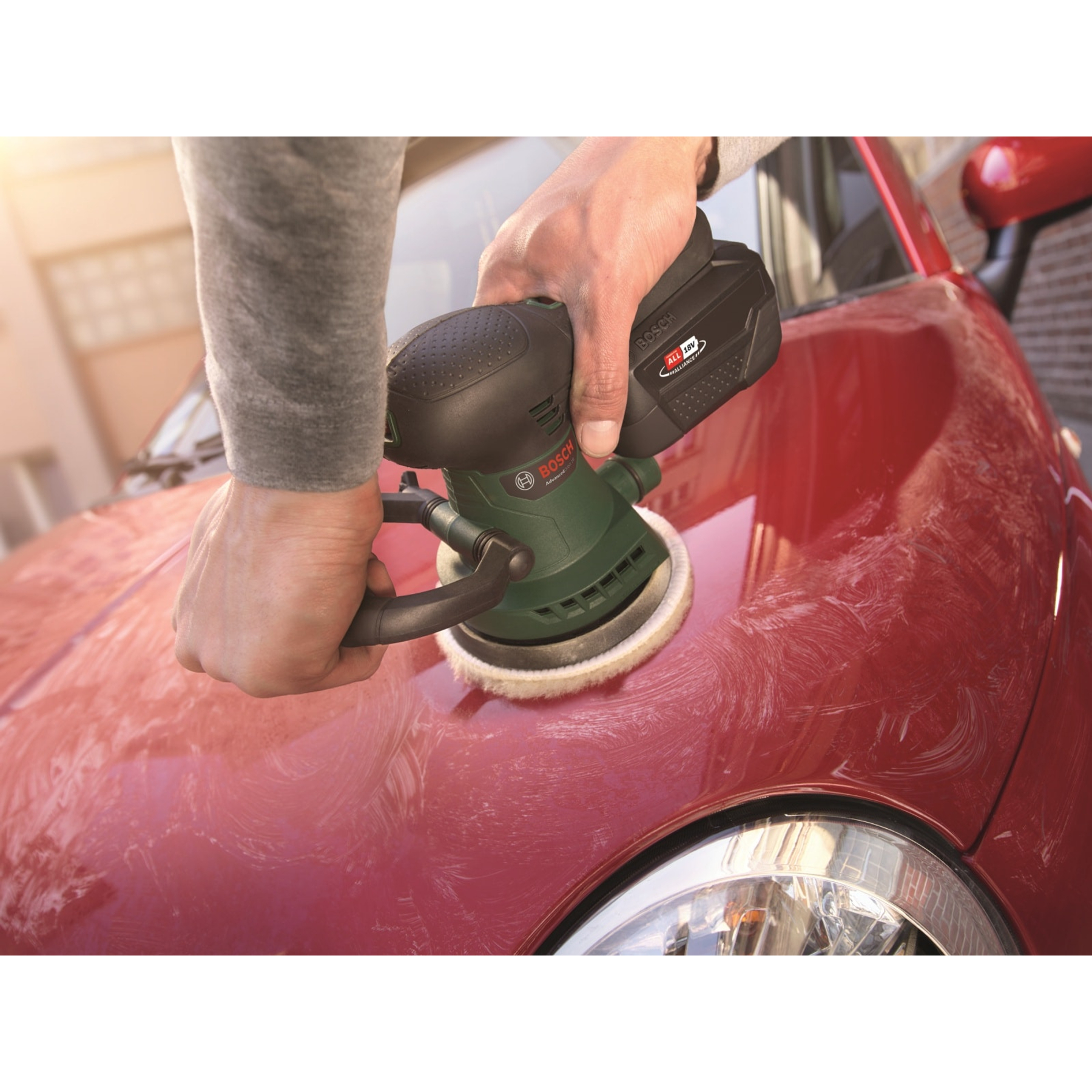 Une personne ponce une voiture rouge avec une ponceuse Bosch verte et noire.