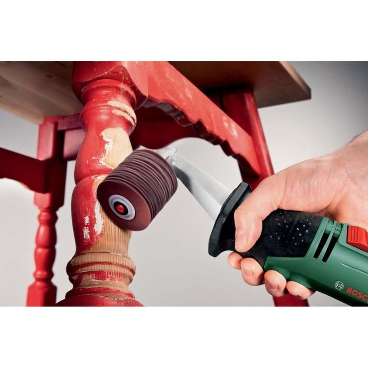 Osoba używa narzędzia szlifierskiego Bosch Texoro na czerwonej nodze stołu.