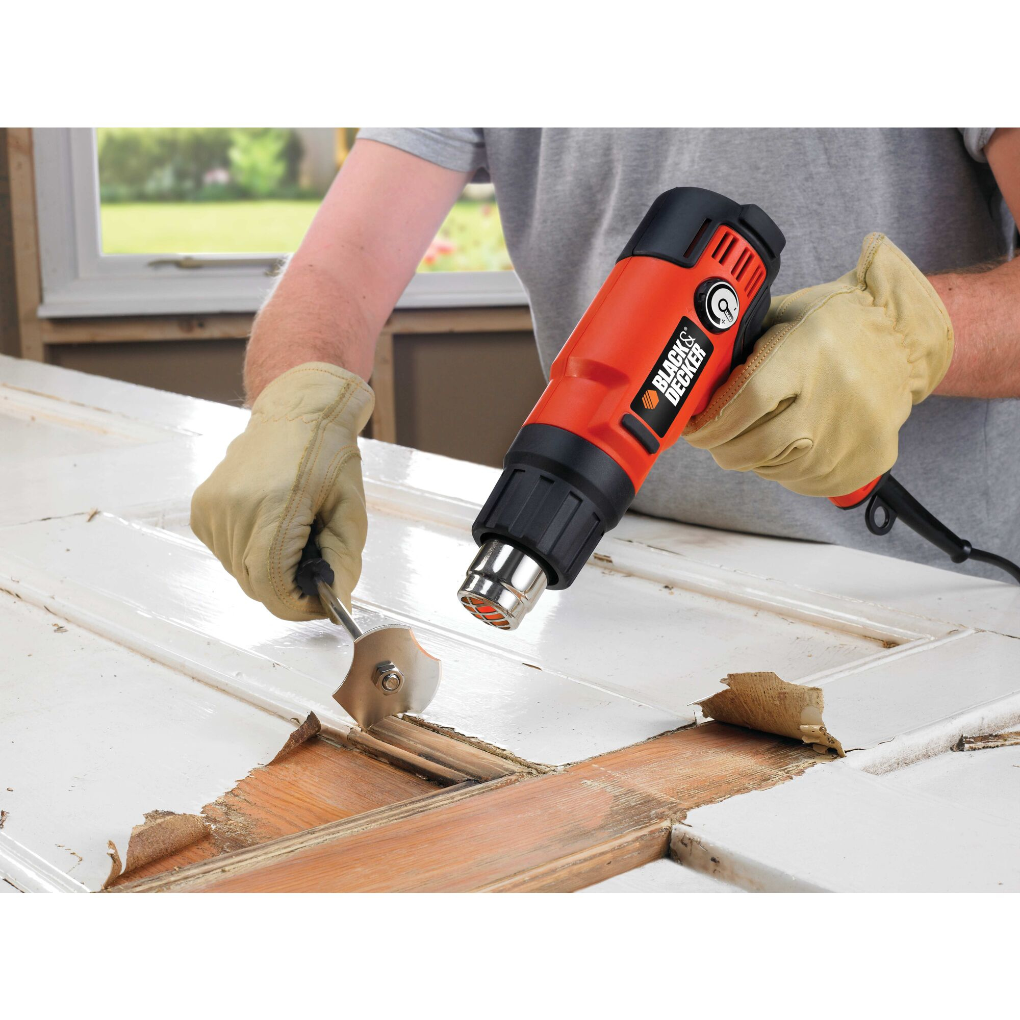 Osoba używa opalarki do usuwania farby z drzwi. Założone rękawice. Widoczna skrobaczka.