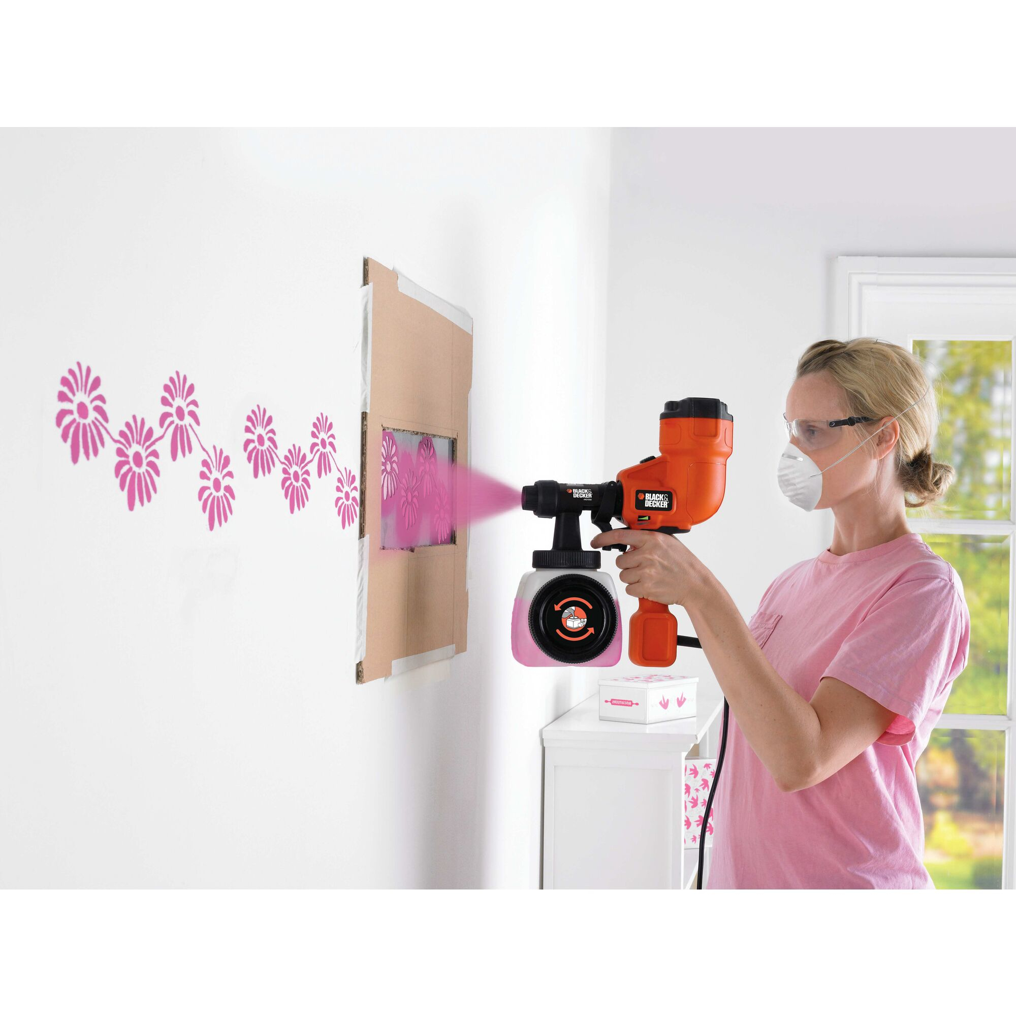 Una persona spruzza vernice rosa con un nebulizzatore, uno stencil e una scala sullo sfondo.
