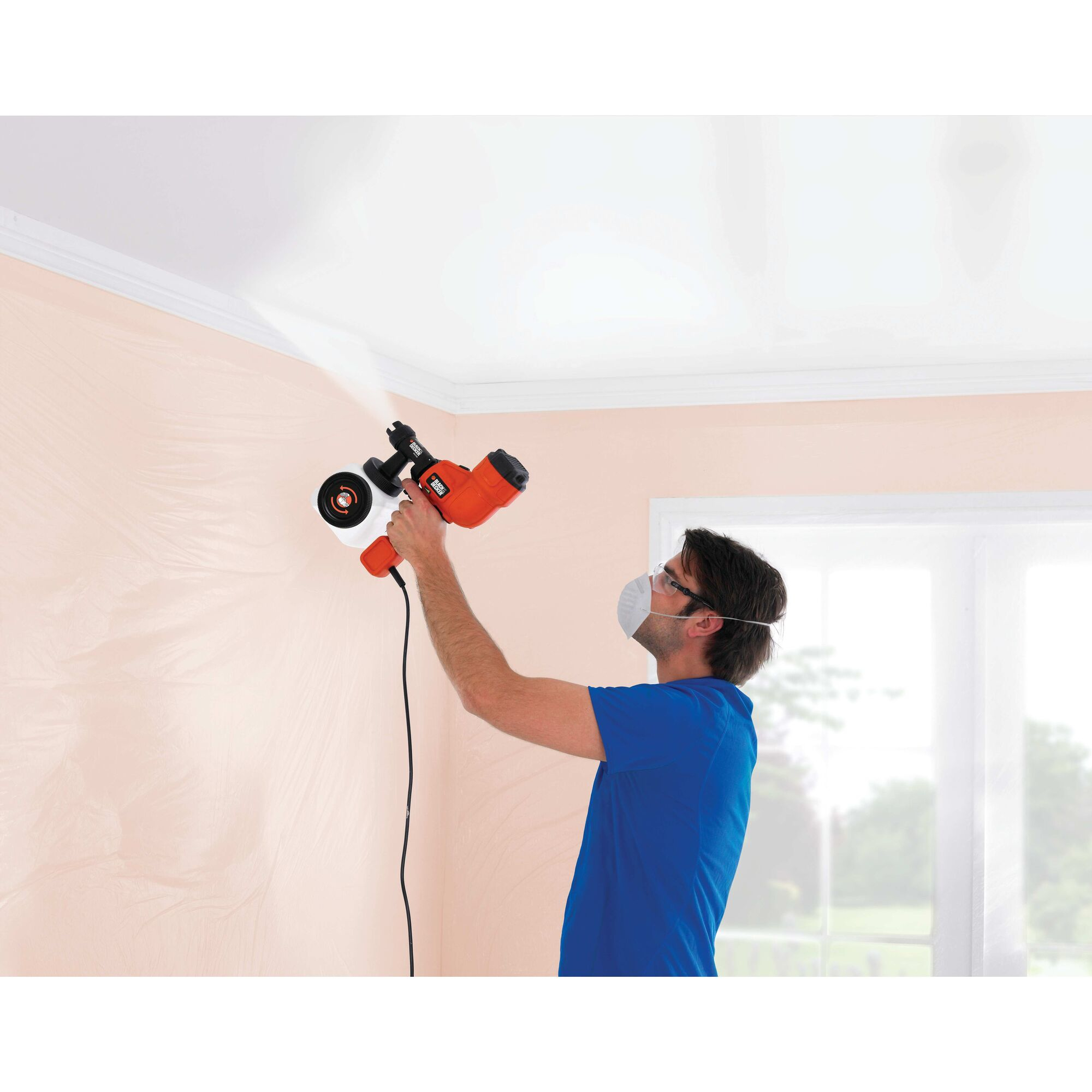 Una persona spruzza un soffitto con un nebulizzatore. Un soffitto bianco, una parete rosa e finestre sono visibili.