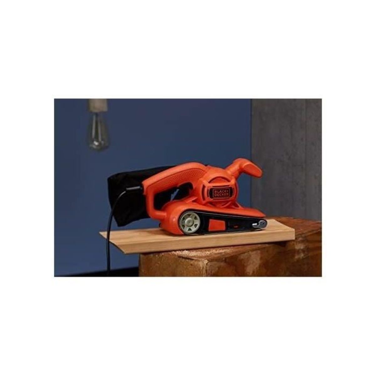 Pomarańczowa szlifierka taśmowa na drewnianej desce. Niebieska ściana w tle. Czarny worek na pył.