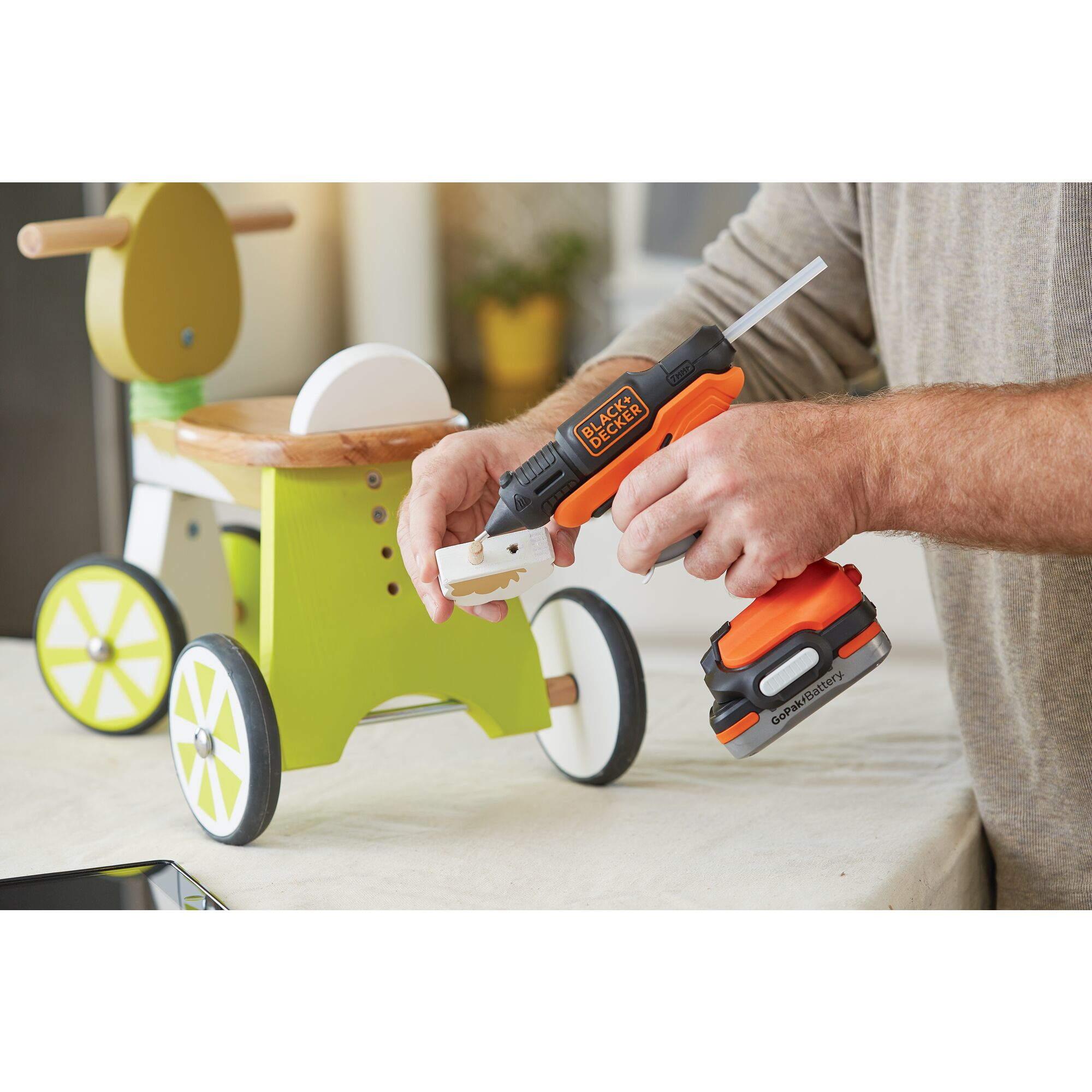Uomo usa pistola colla arancione per attaccare pezzo a giocattolo legno. Batteria attaccata.