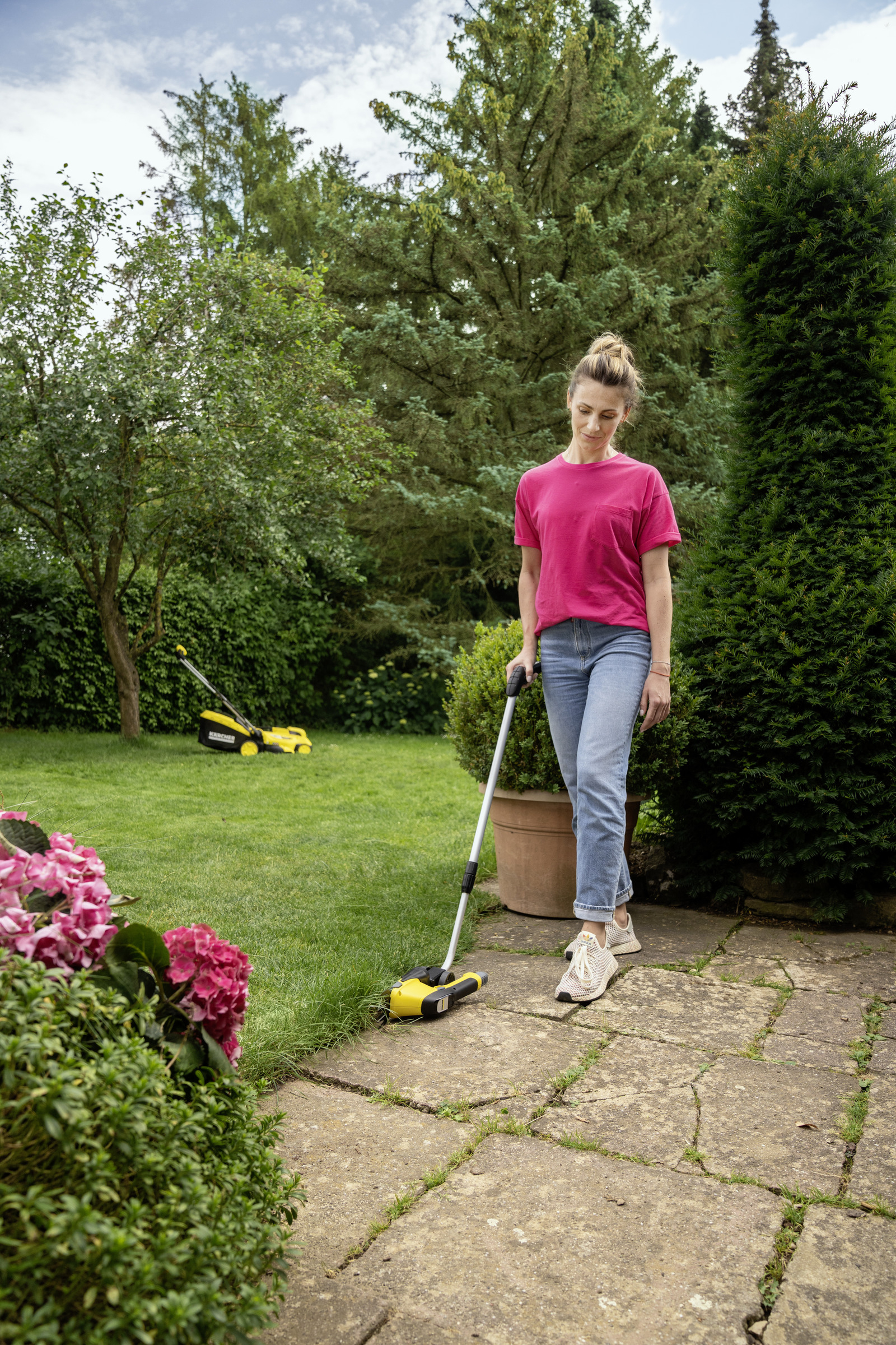 Frau mit einem Rasenkantenstecher auf einem gepflasterten Weg im Garten.