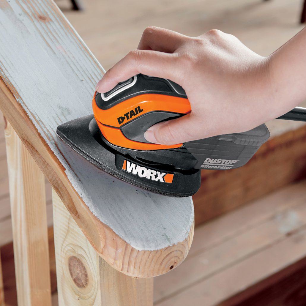 Una persona che leviga una ringhiera di legno con una levigatrice Worx D-Tail. La ringhiera è in legno chiaro.