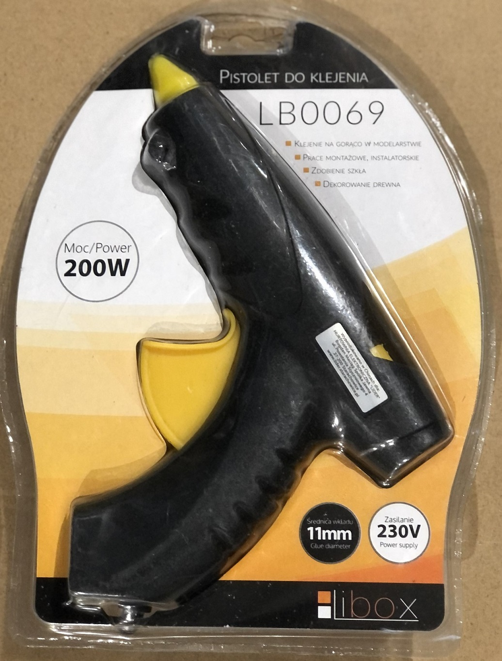 Pistola per colla nera nella sua confezione. Grilletto giallo. Include dettagli e specifiche del prodotto.