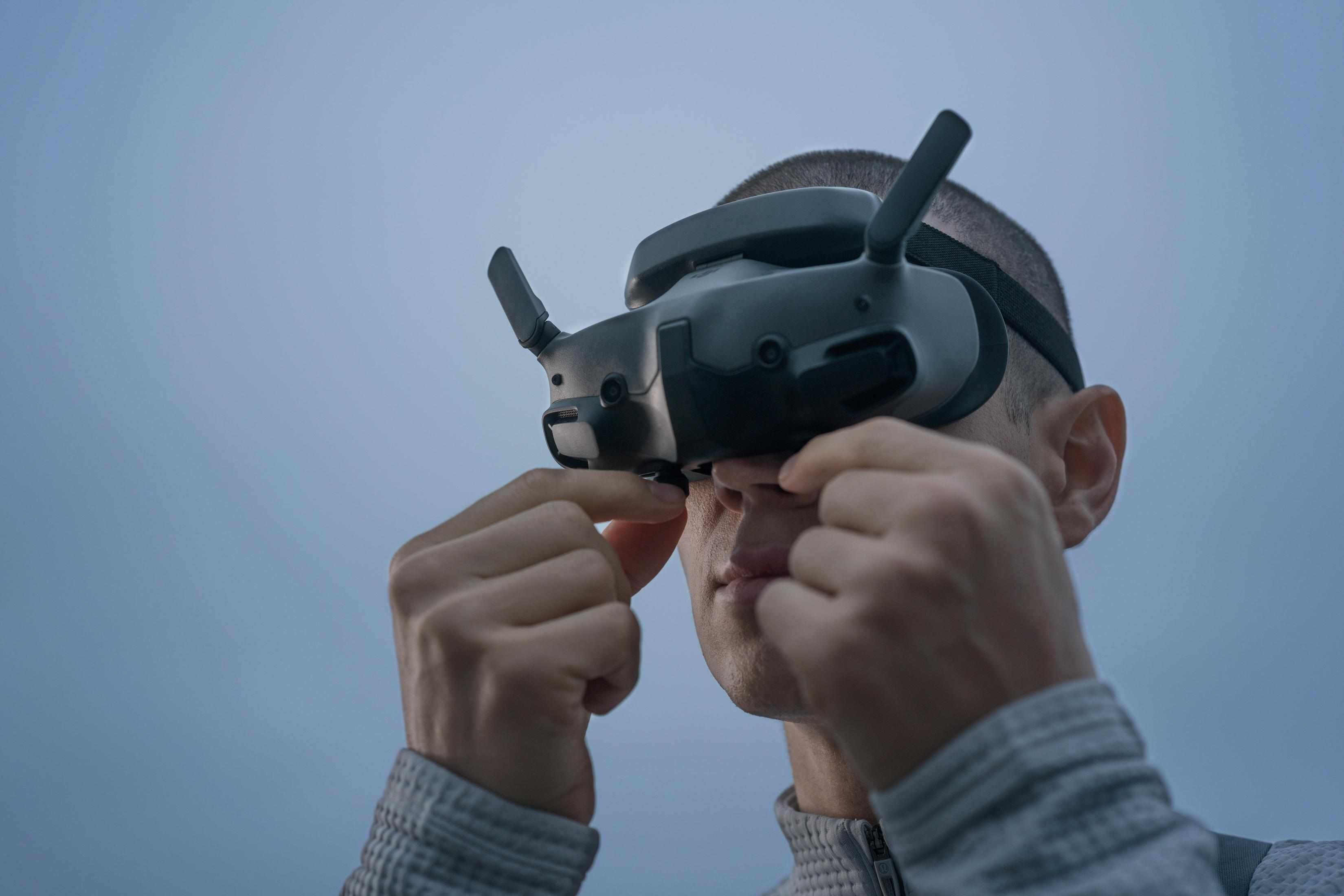 Uomo che regola il visore VR, primo piano. Mani vicino al viso, cielo blu-grigio.
