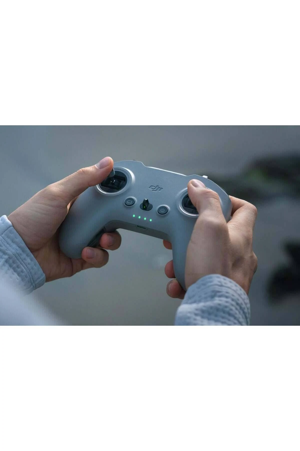 Dłonie trzymające szary kontroler drona DJI. Widoczne przyciski i joysticki.