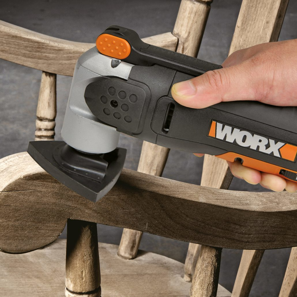 Una mano che usa un utensile WORX Sonicrafter per levigare un braccio curvo di una sedia in legno.