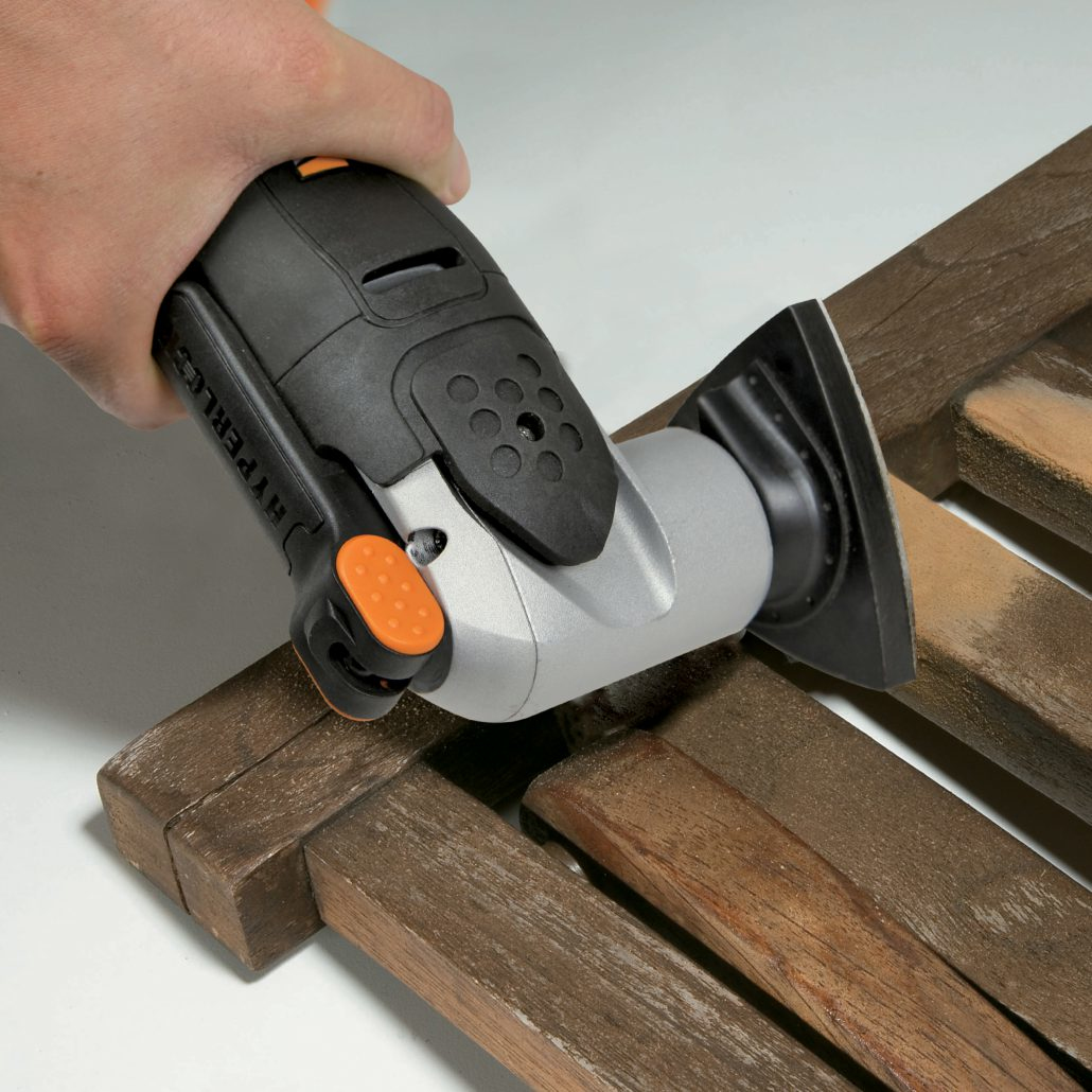 Una mano tiene un utensile oscillante nero e grigio che leviga una superficie di legno. L'utensile ha accenti arancioni.