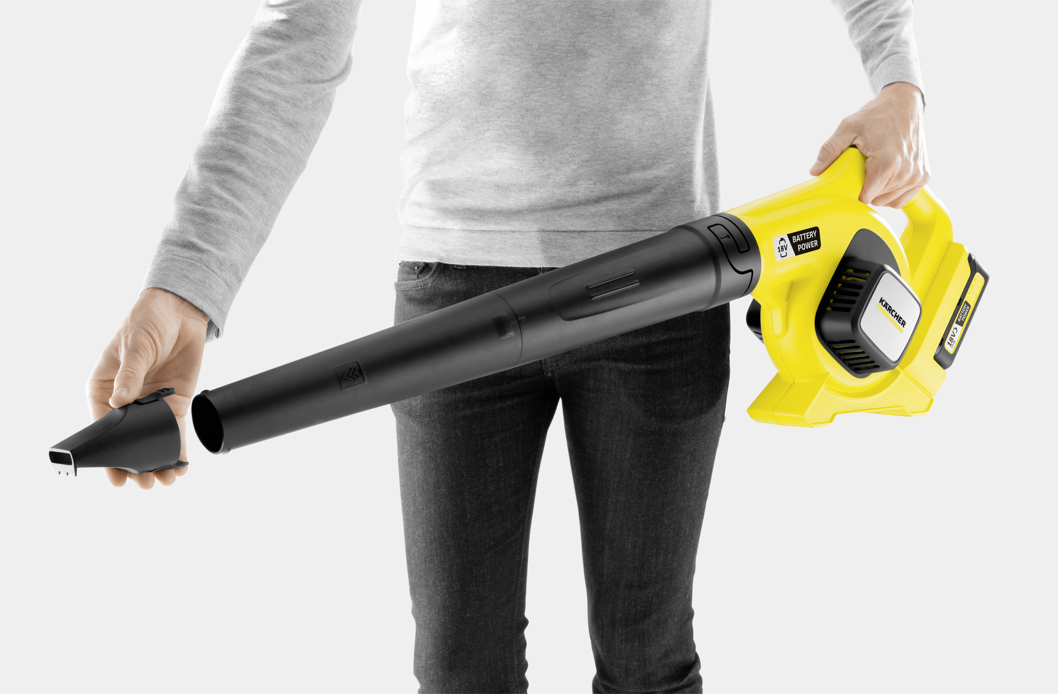 Osoba podłącza dyszę do żółtej dmuchawy do liści. Szare tło.